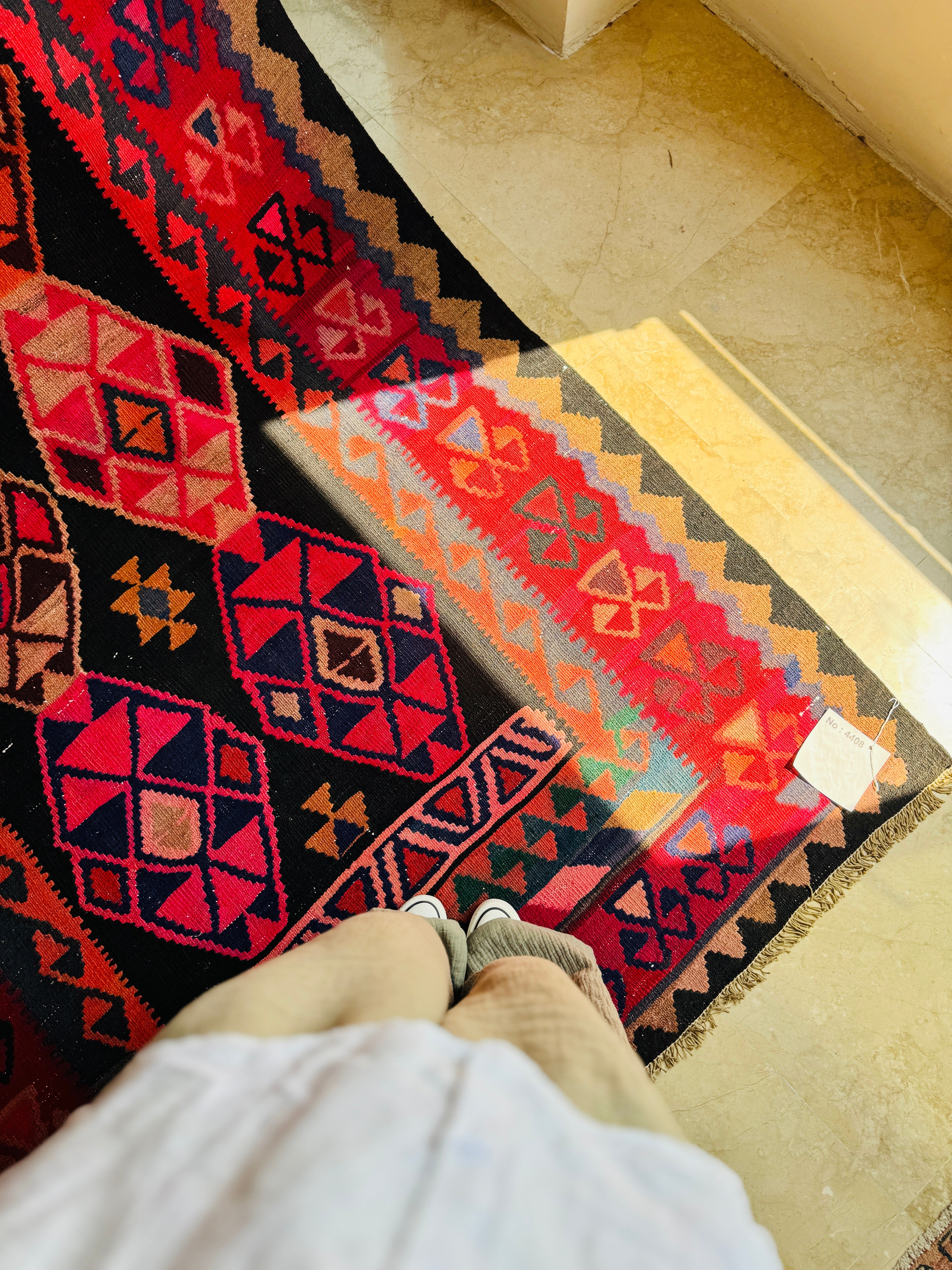 Overhead lifestyle shot of a person standing on the red and black kilim rug.