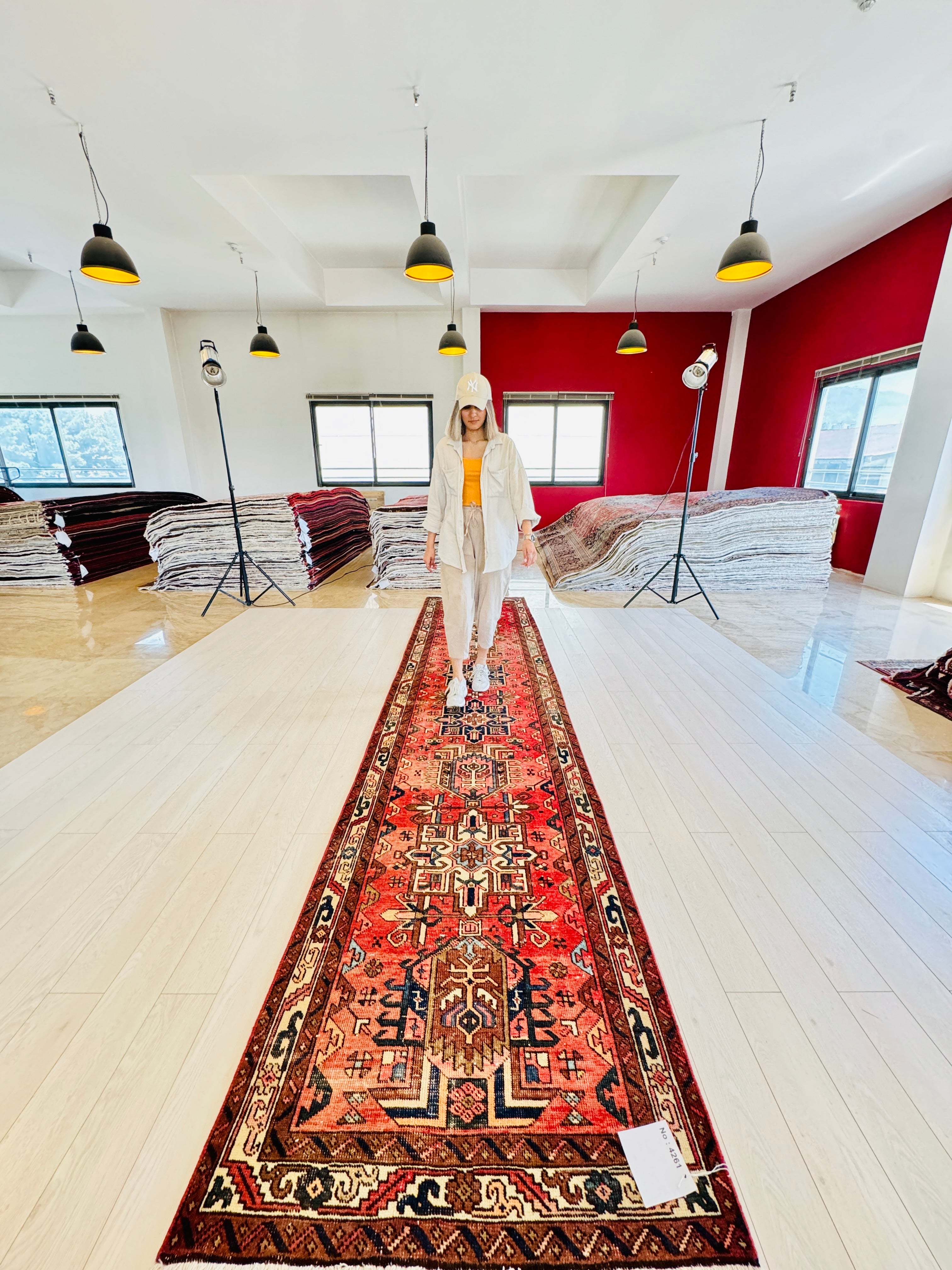 Model standing on Hand-Knotted Antique Wool Runner Rug – 14' 9" x 3' 4" in a showroom, highlighting the rug's scale and vibrant geometric design.