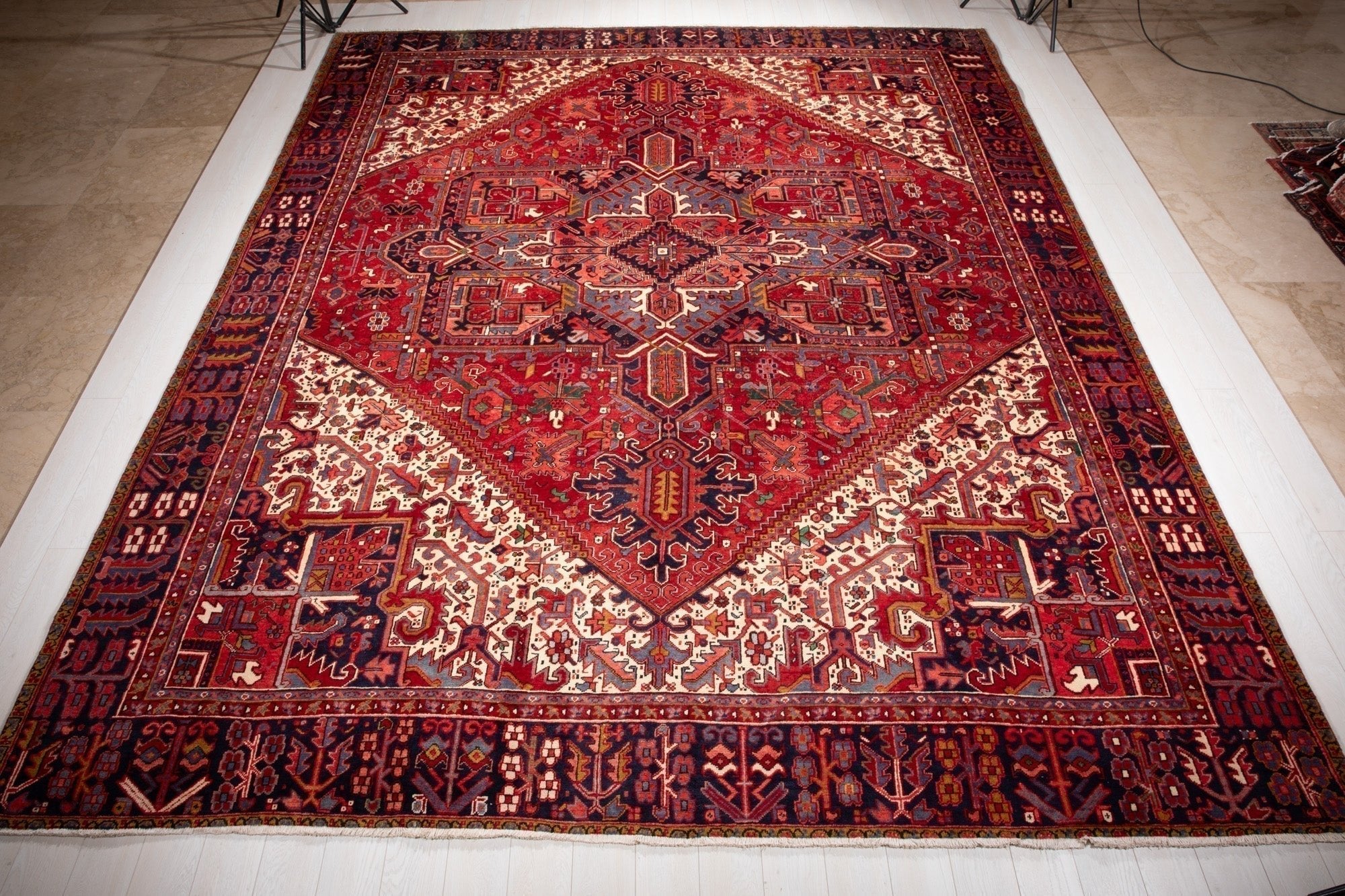 Full view of the large red Persian Heriz rug with a diamond medallion on cream corners.