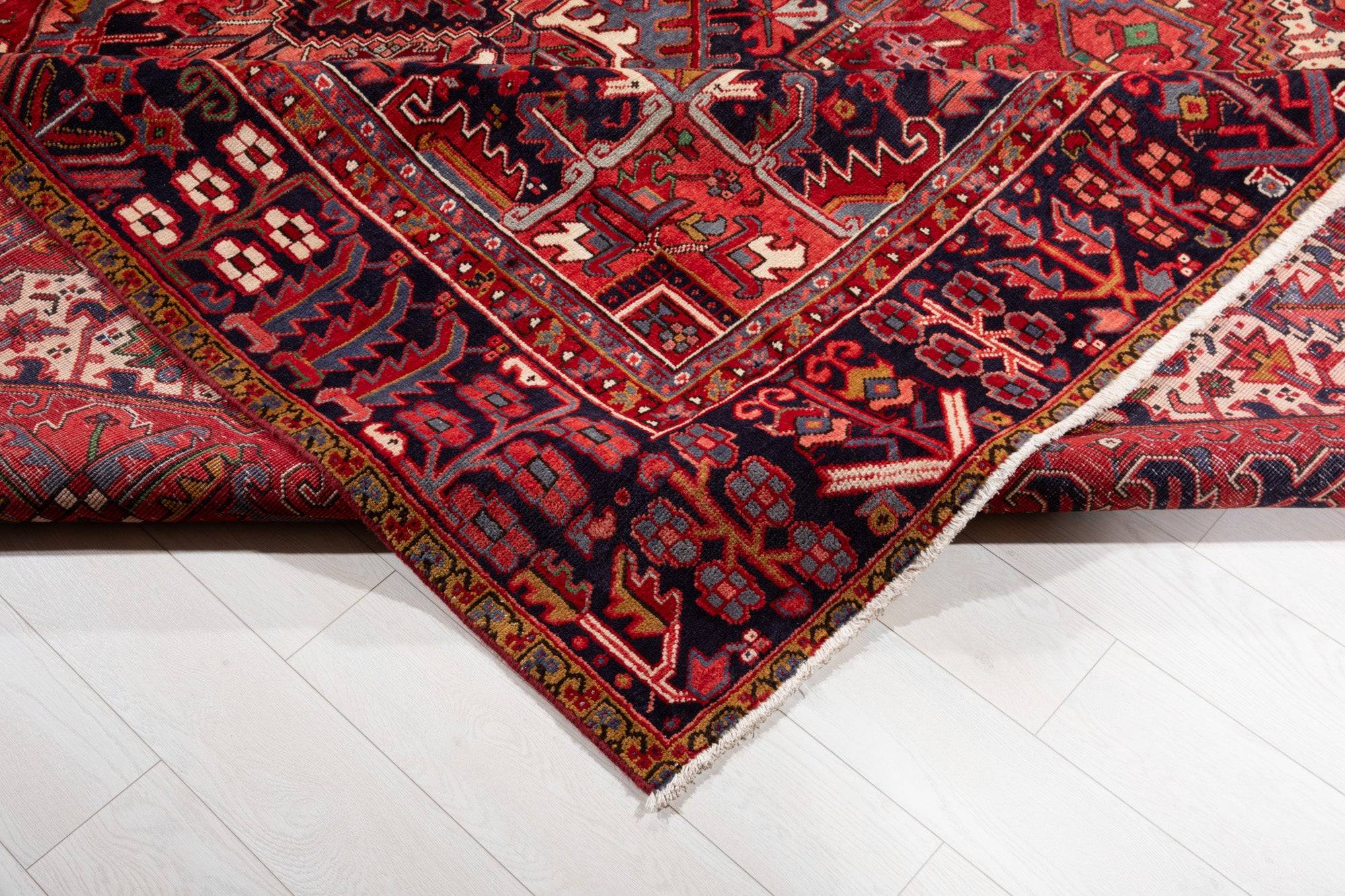 Corner of the rug folded up on a wood floor, showing the border pattern and fringe.