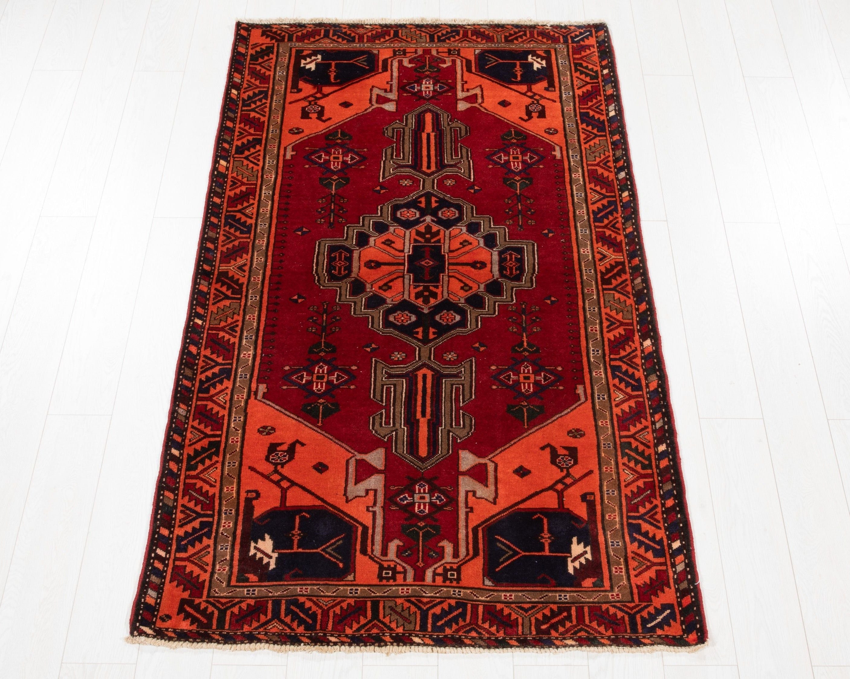 Full view of the red and orange Persian tribal rug with a navy geometric medallion.