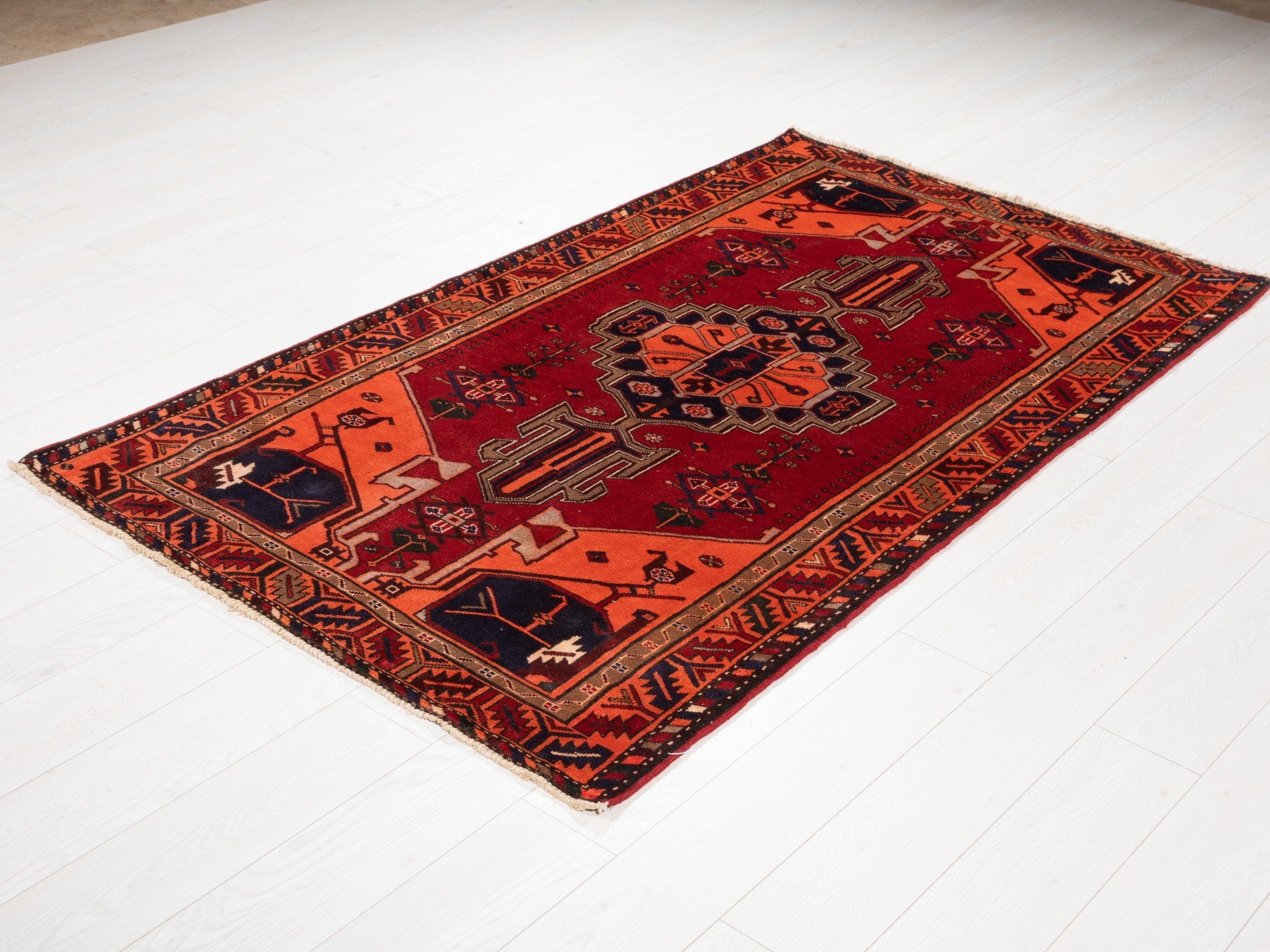 Angled view of the full rug on a white floor, showing the red-orange medallion design.