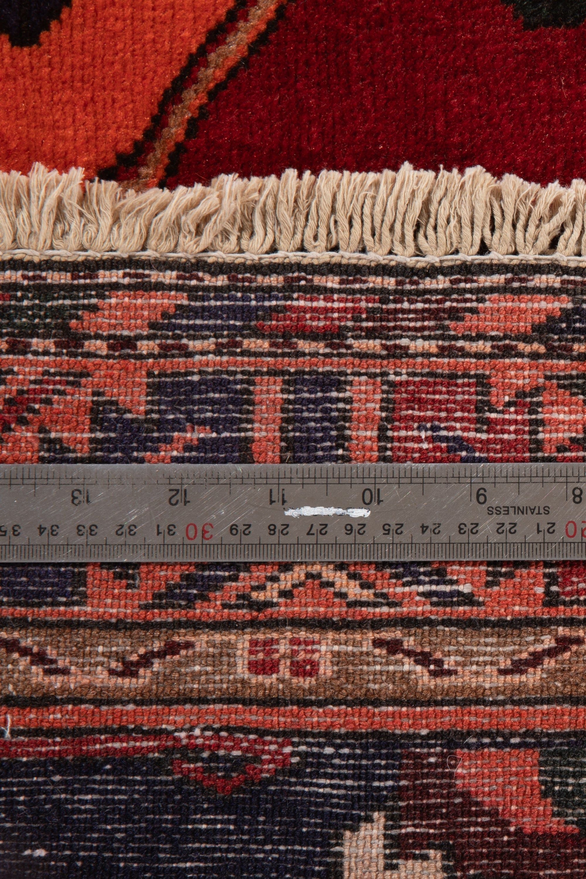 Measuring tape across the rug's end, showing the fringe and geometric border pattern.
