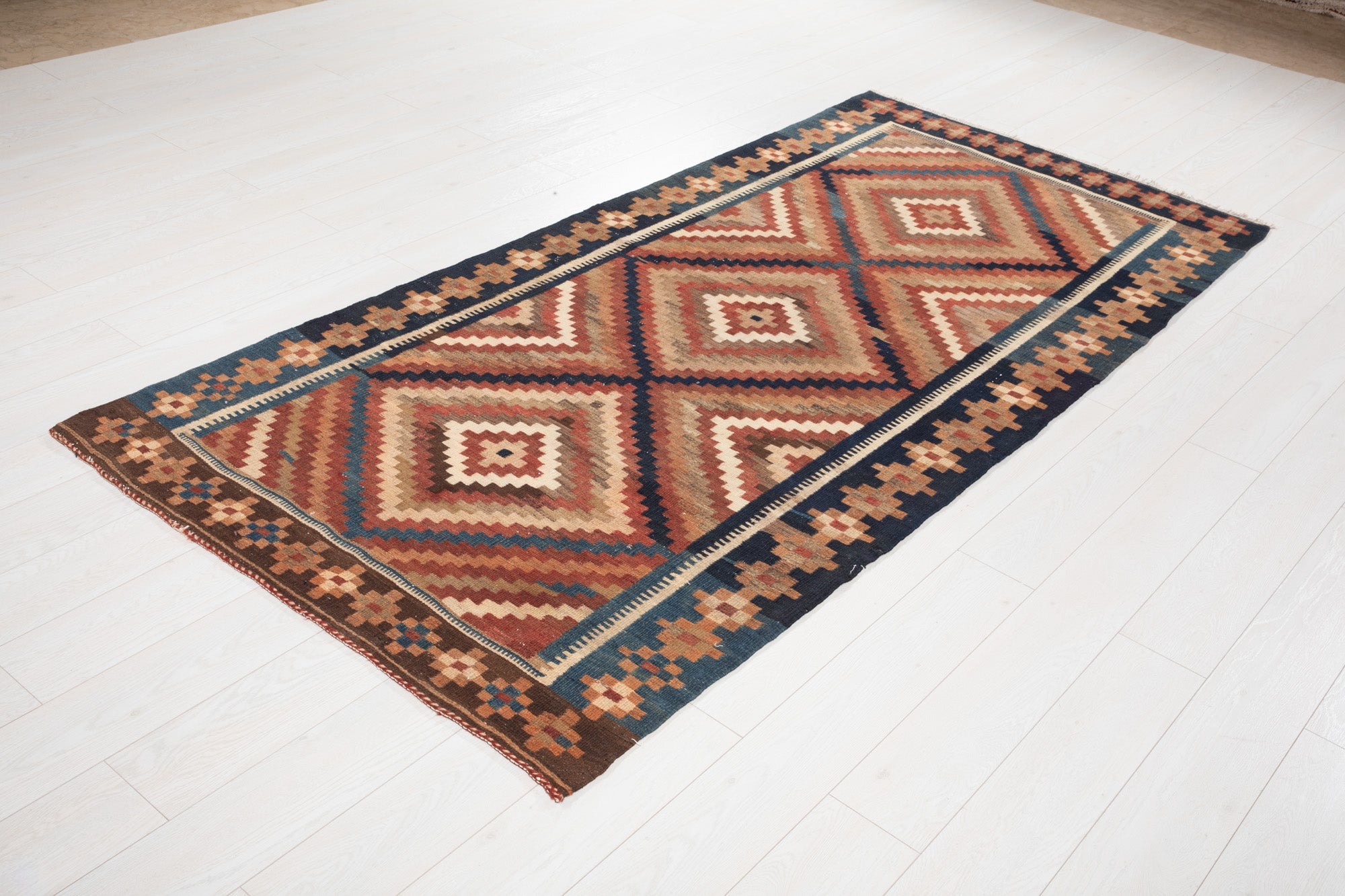 Angled view of the full kilim rug on a white floor, showing the diamond pattern.