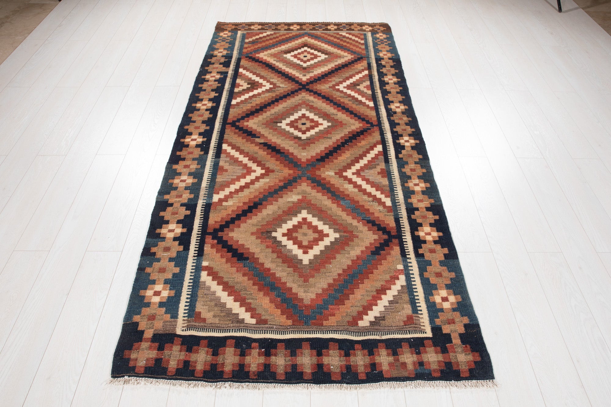 Straight-on full view of the kilim rug showing the checkerboard end border and fringe.