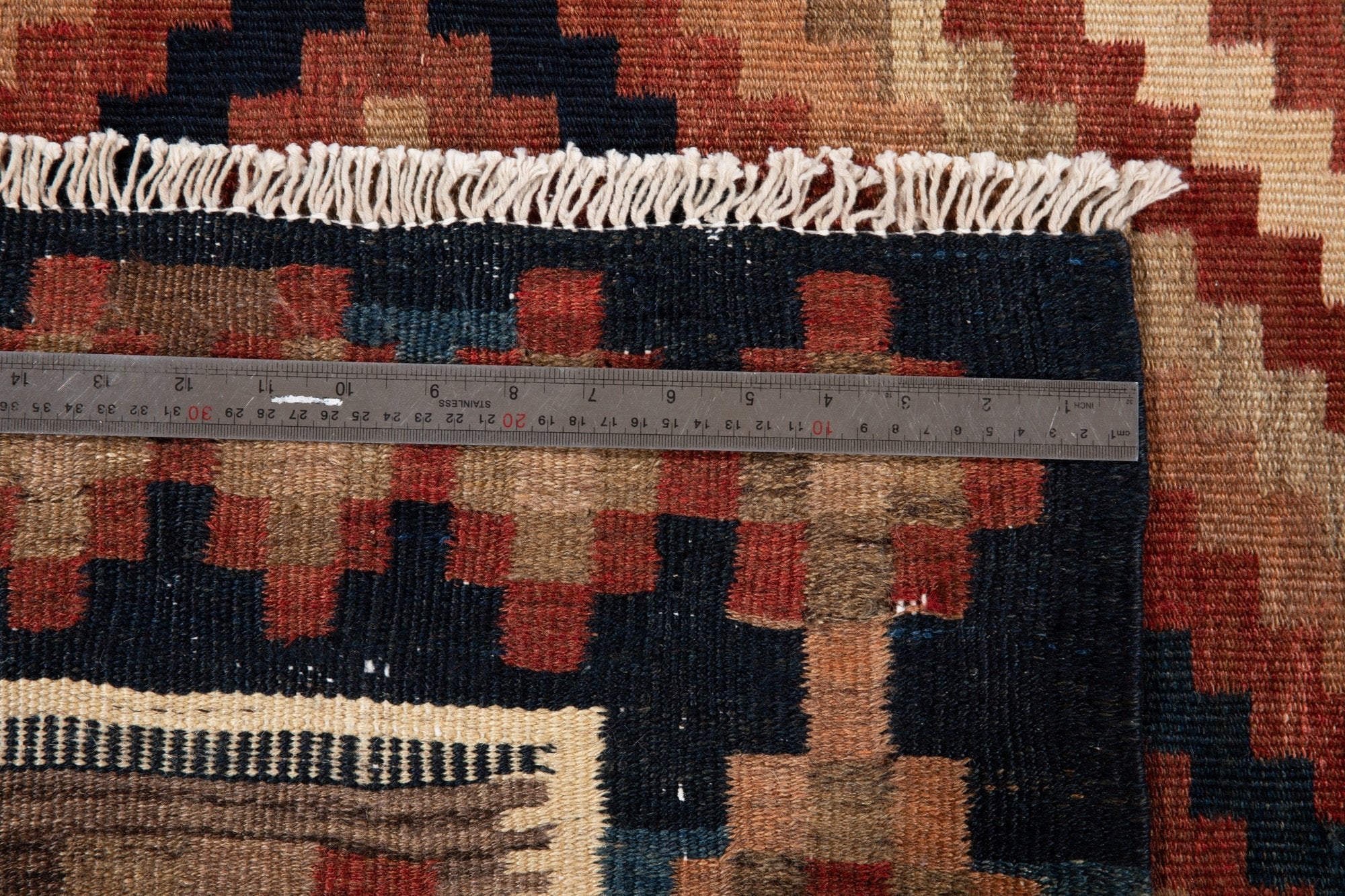 Measuring tape across the checkerboard end border, showing fringe detail.