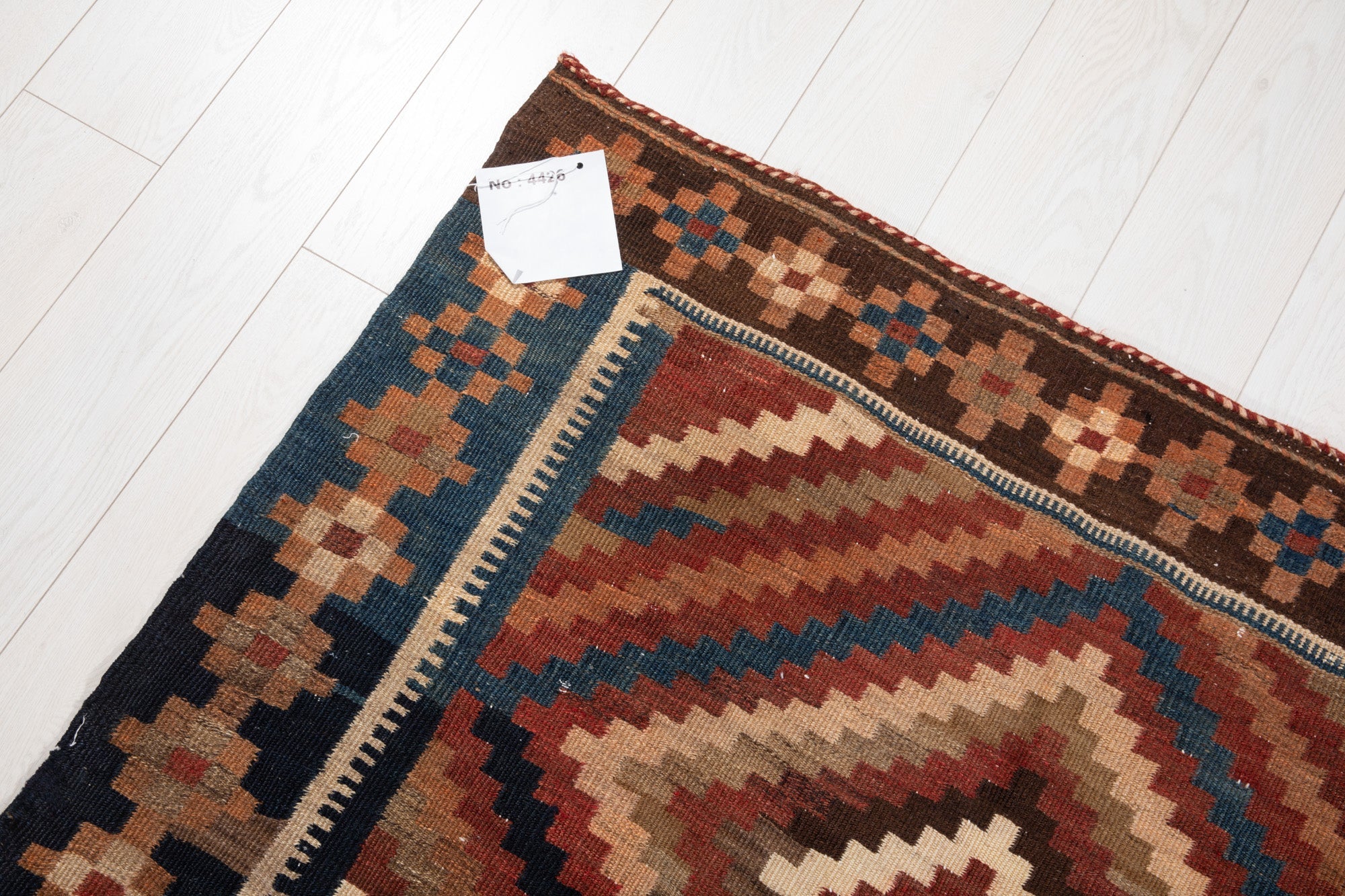 Corner of the kilim with an attached inventory tag showing its rug number.