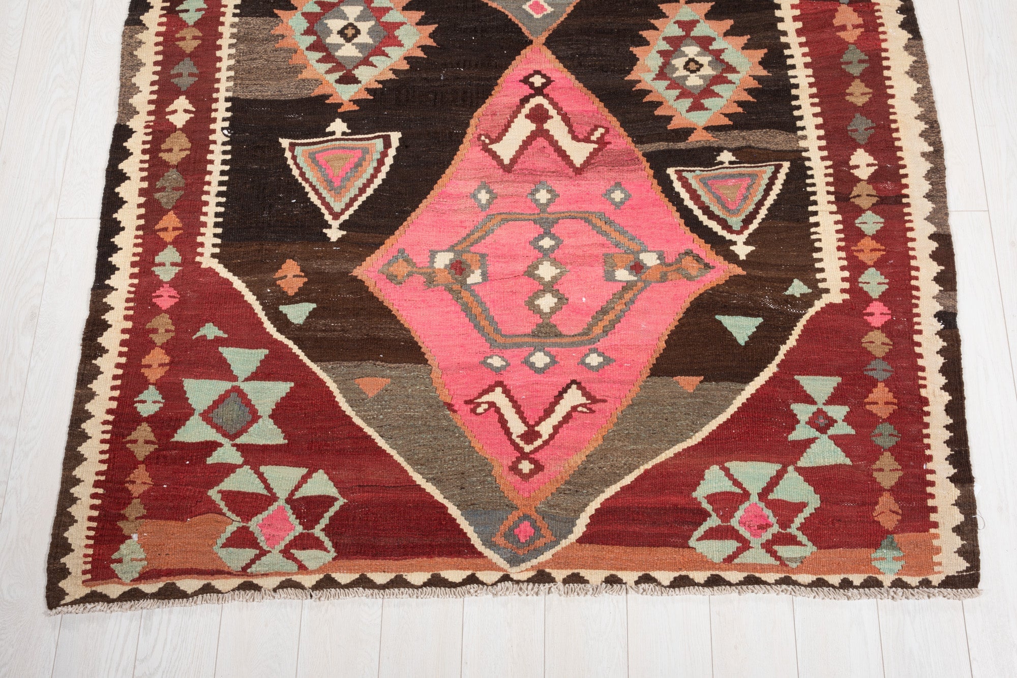 One end of the vintage kilim runner showing a pink diamond medallion and fringed edge.
