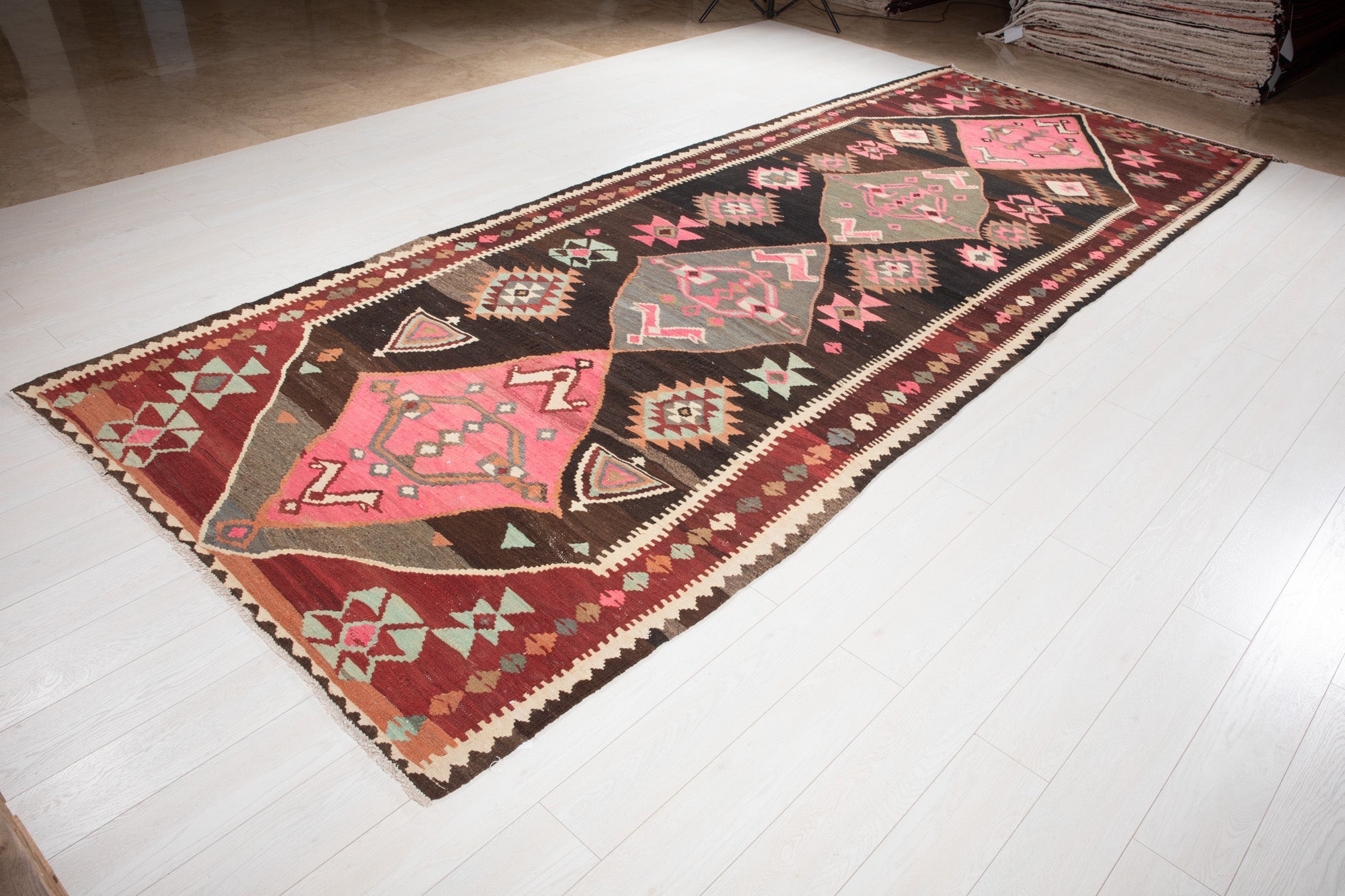 Angled view of the vintage kilim runner on the showroom floor, highlighting its pink diamond medallions.