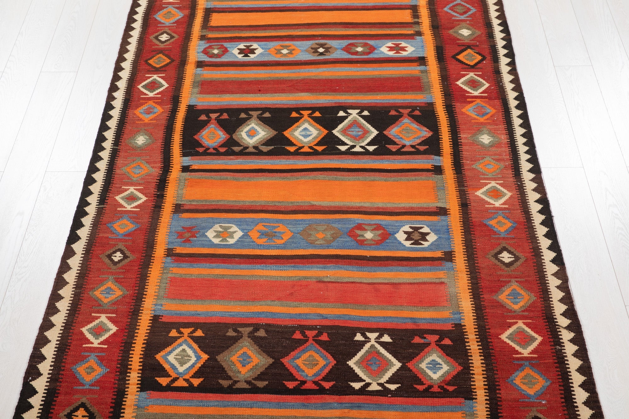 Top-down straight view of the Persian kilim's striped bands and diamond motifs.