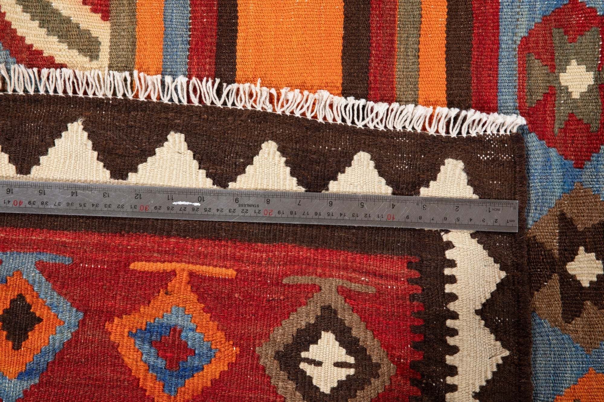 Ruler measuring the kilim's zigzag border next to the fringed edge.