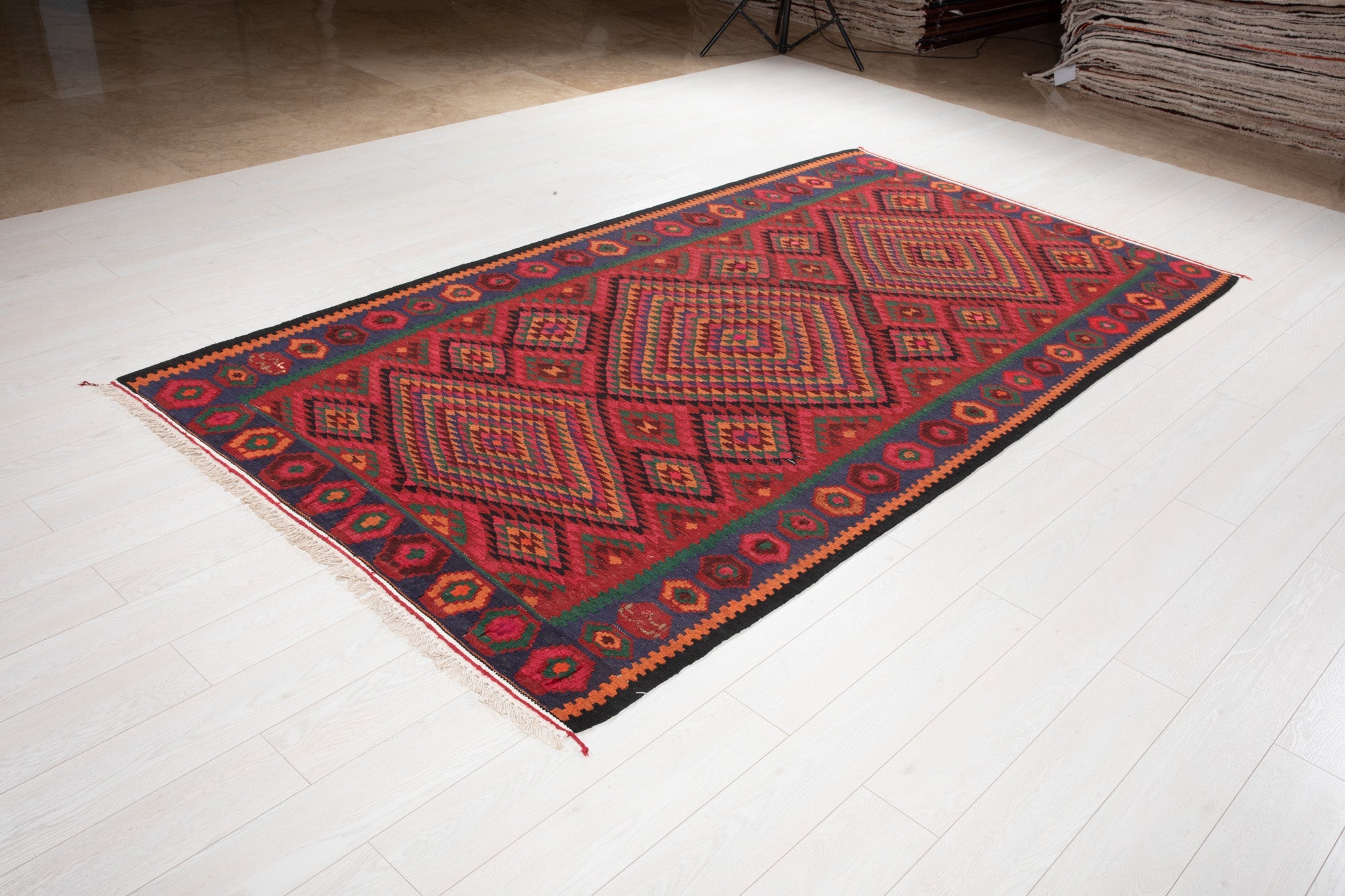 Angled view of the red Persian kilim rug's geometric diamond design on the showroom floor.