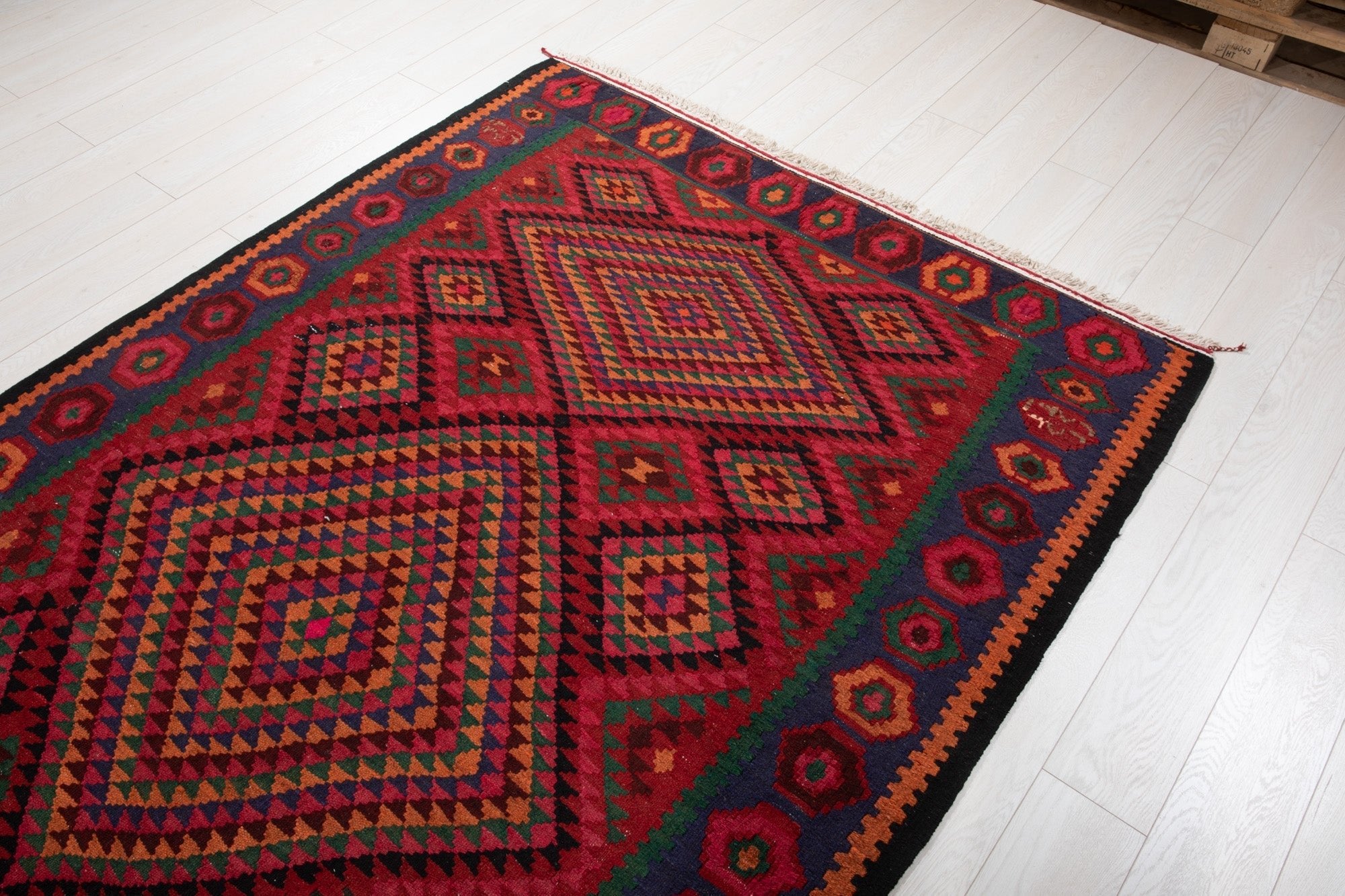 Warehouse angle shot of the red kilim rug with wood pallets visible in the background.