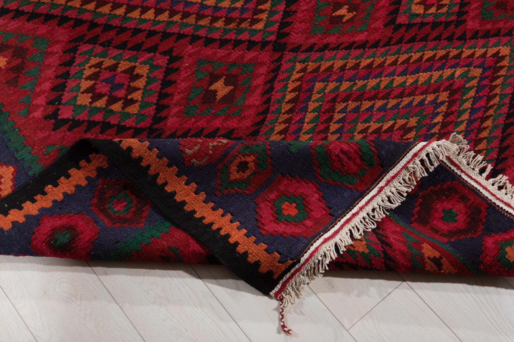 Corner of the kilim rug folded to show its border pattern and fringed edge.