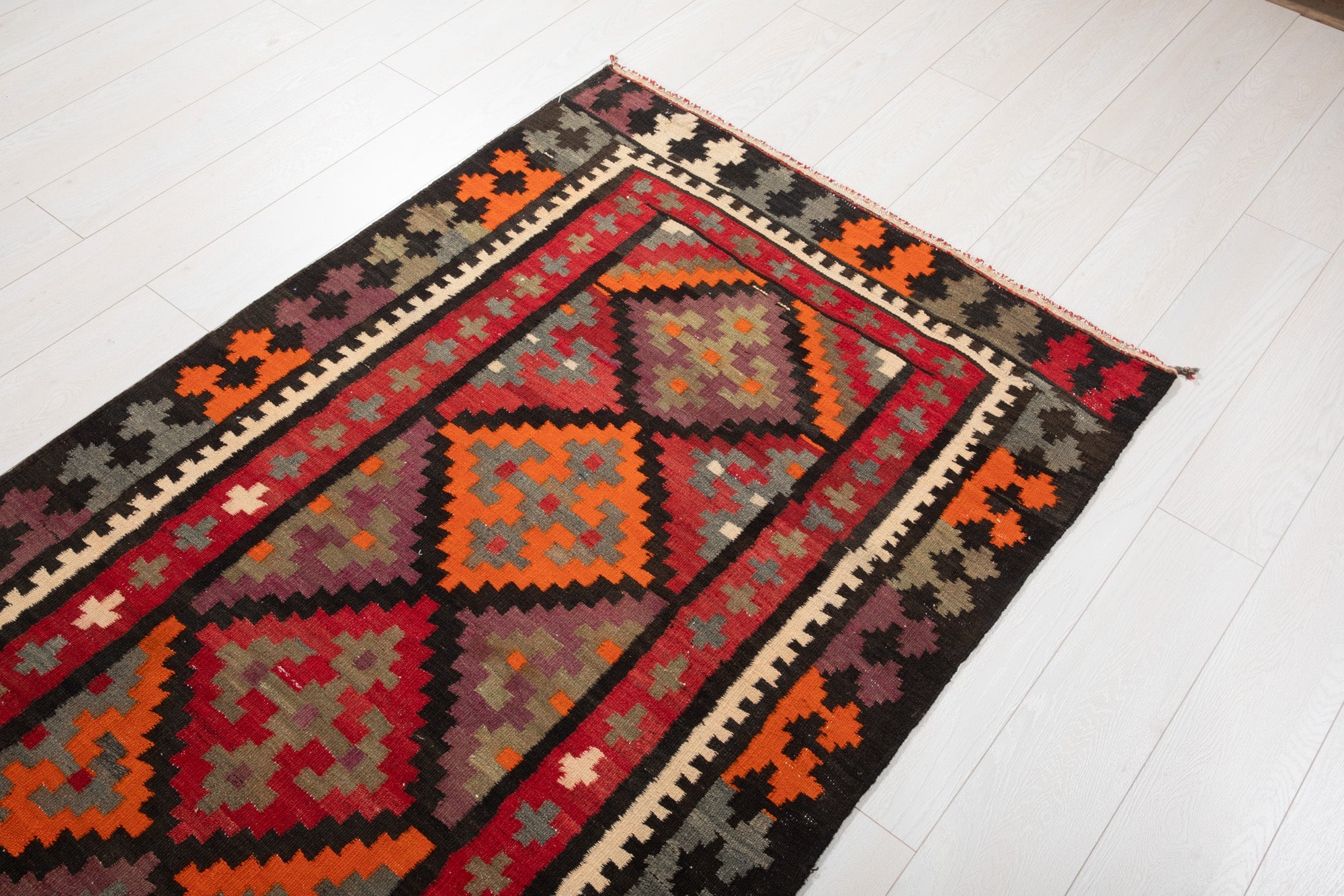 Floor-level angled view of the kilim rug's cross motifs and diamond border.