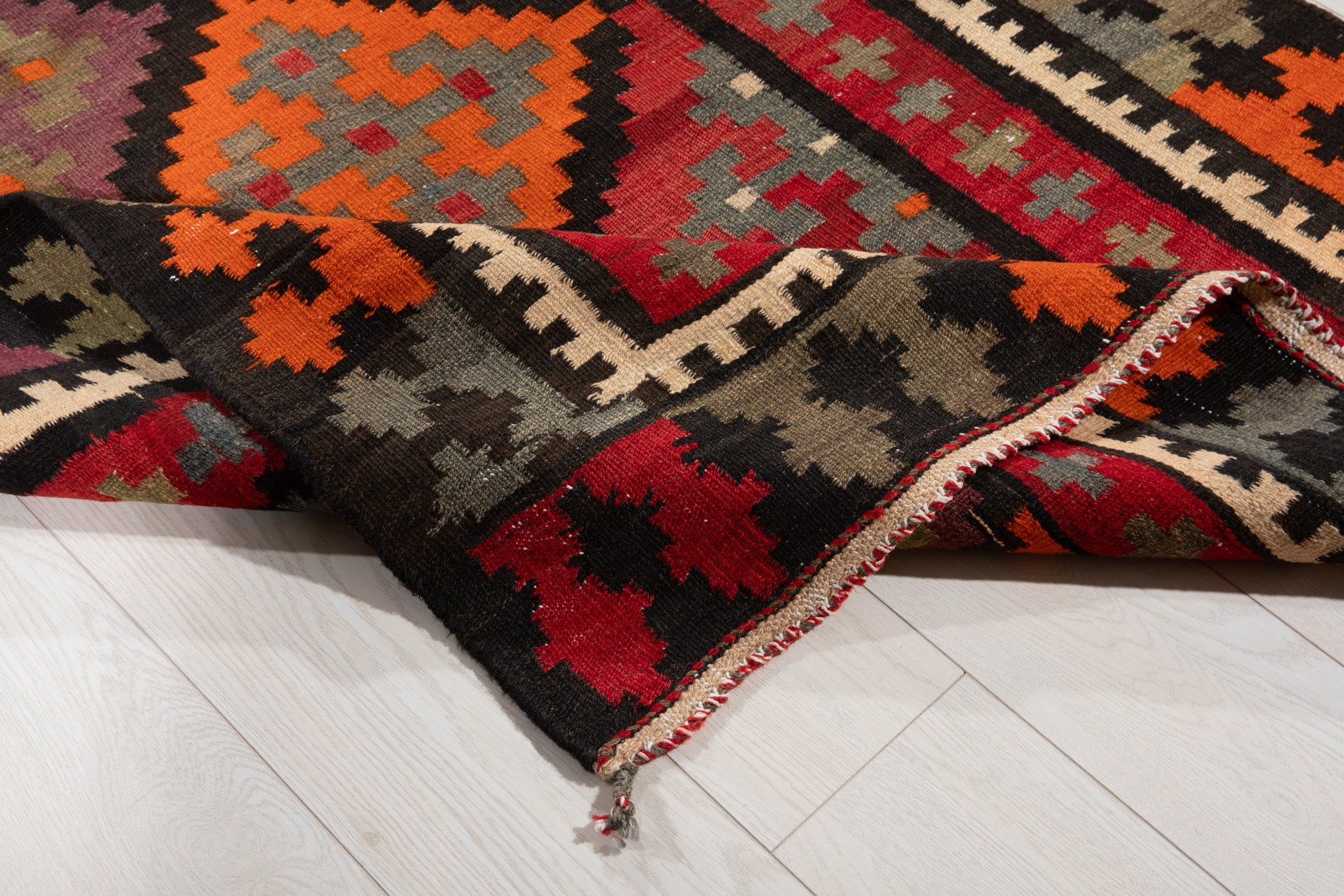 Corner of the kilim runner folded up, revealing its fringed edge and border.
