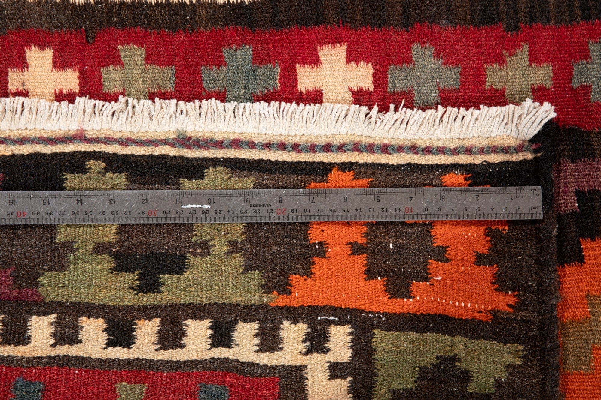Ruler measuring the kilim's fringe and cross-motif border width.