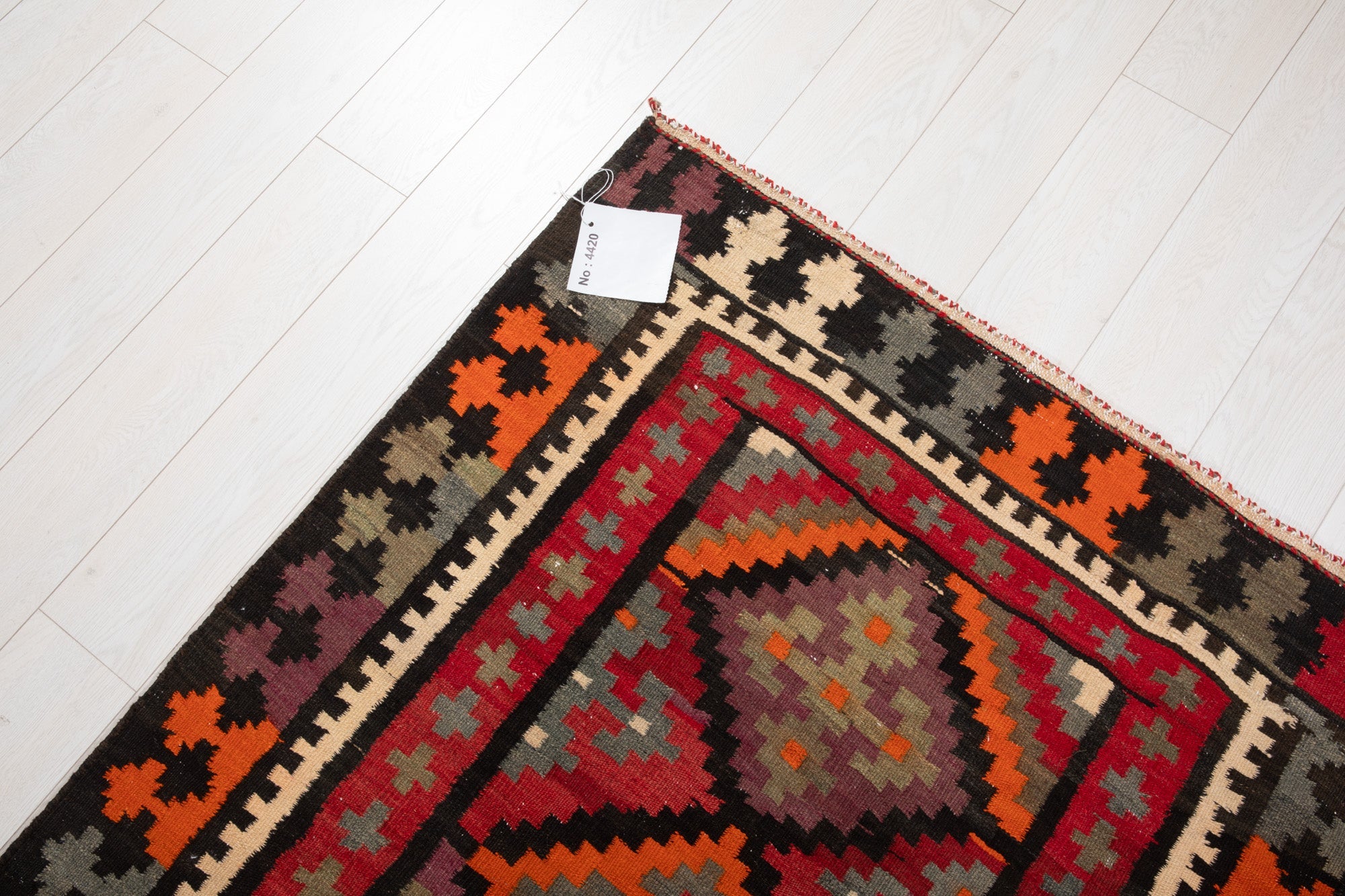 Corner of the vintage Persian kilim rug with an attached inventory identification tag.