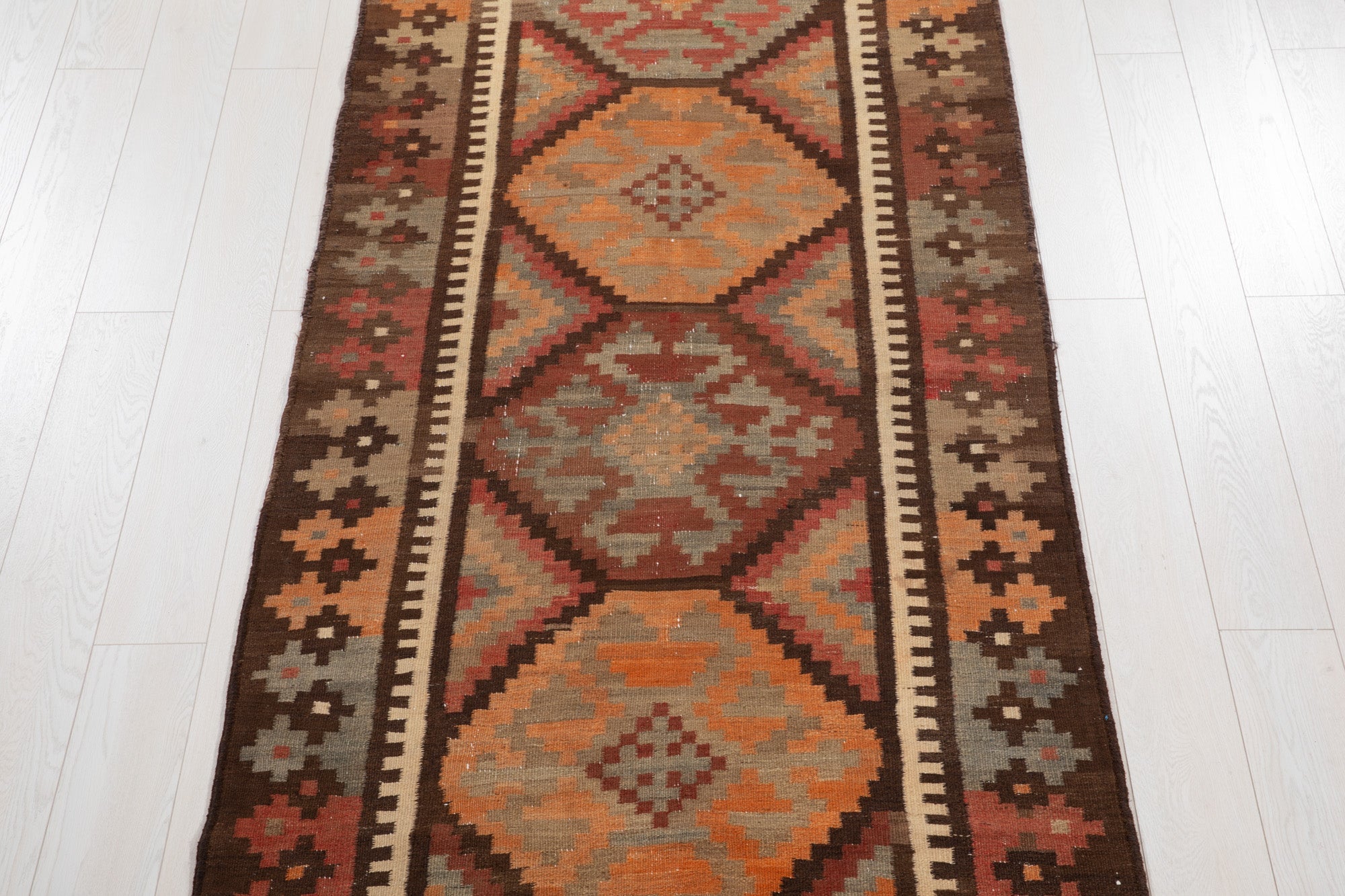 Top-down view of the kilim's stacked diamond medallions in rust and orange tones.