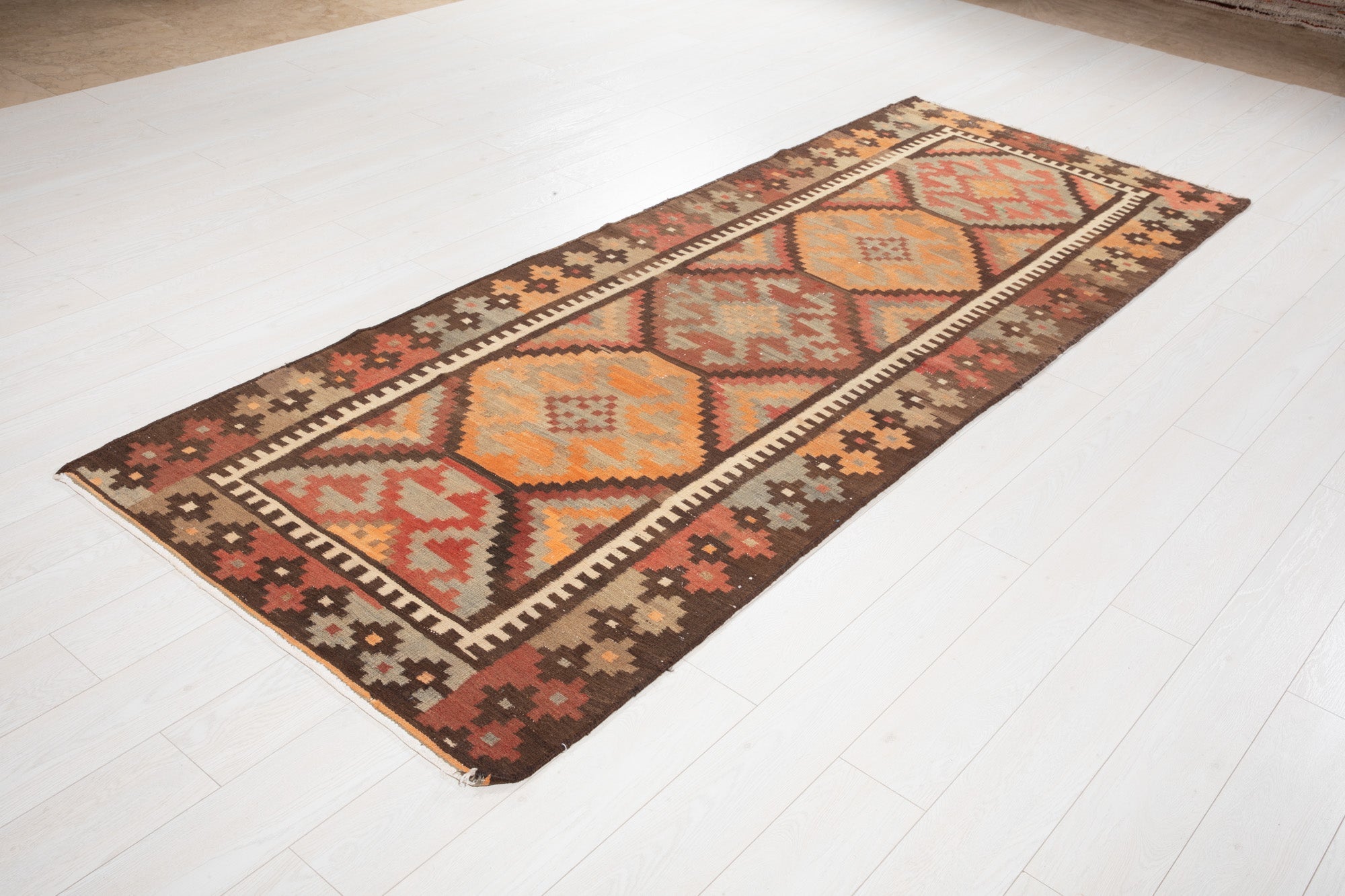 Angled view of the antique kilim runner's orange diamond medallions on a wood floor.