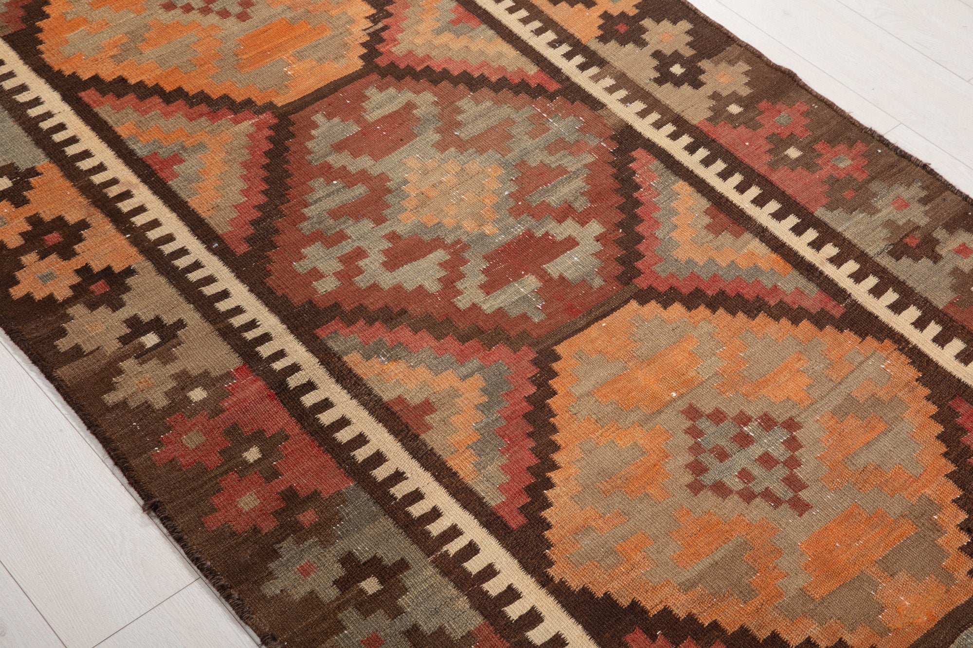 Diagonal close view of the kilim's orange and rust diamond medallions.