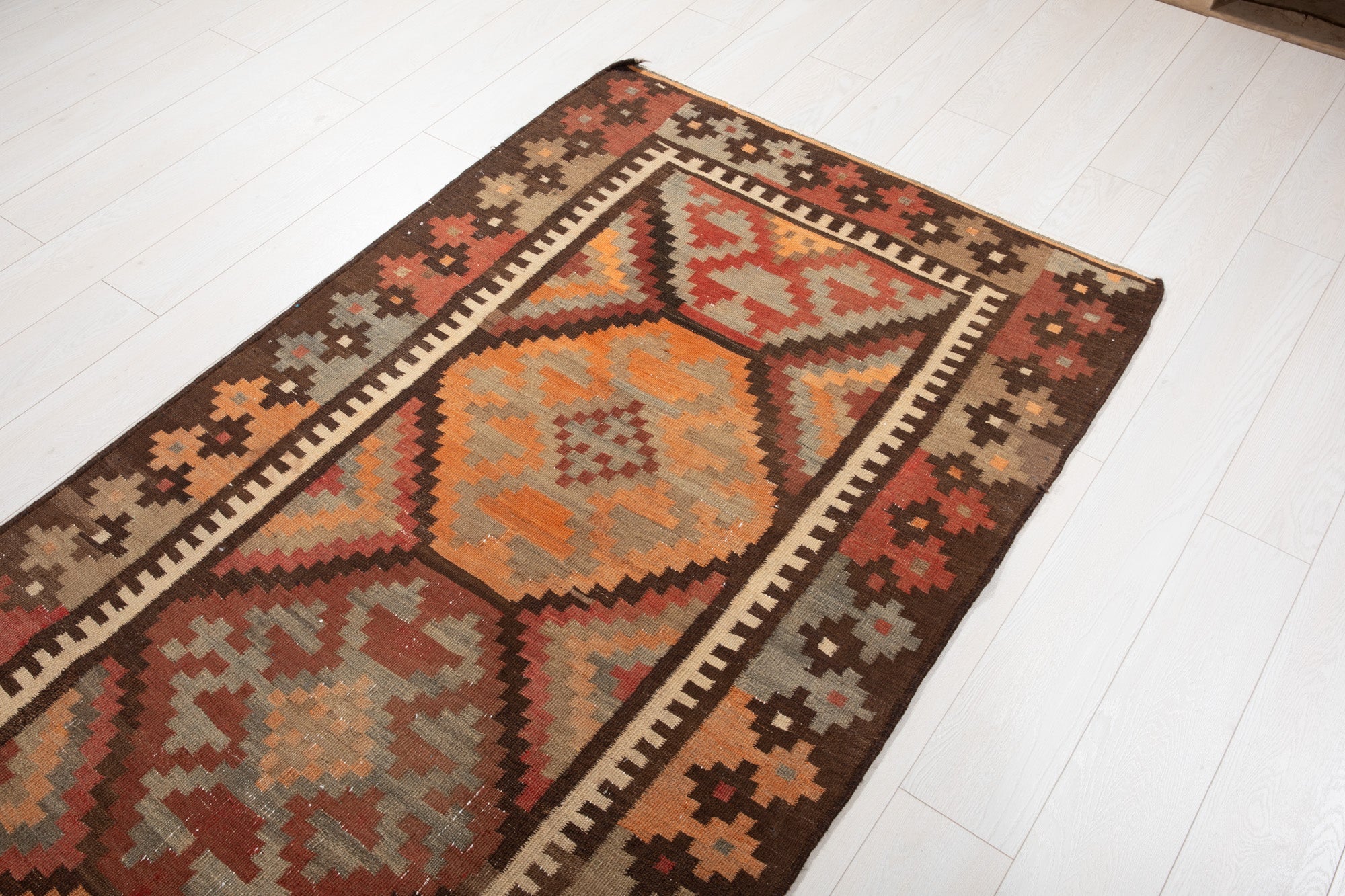 Floor-level angled view of the kilim's diamond medallions and zigzag border.