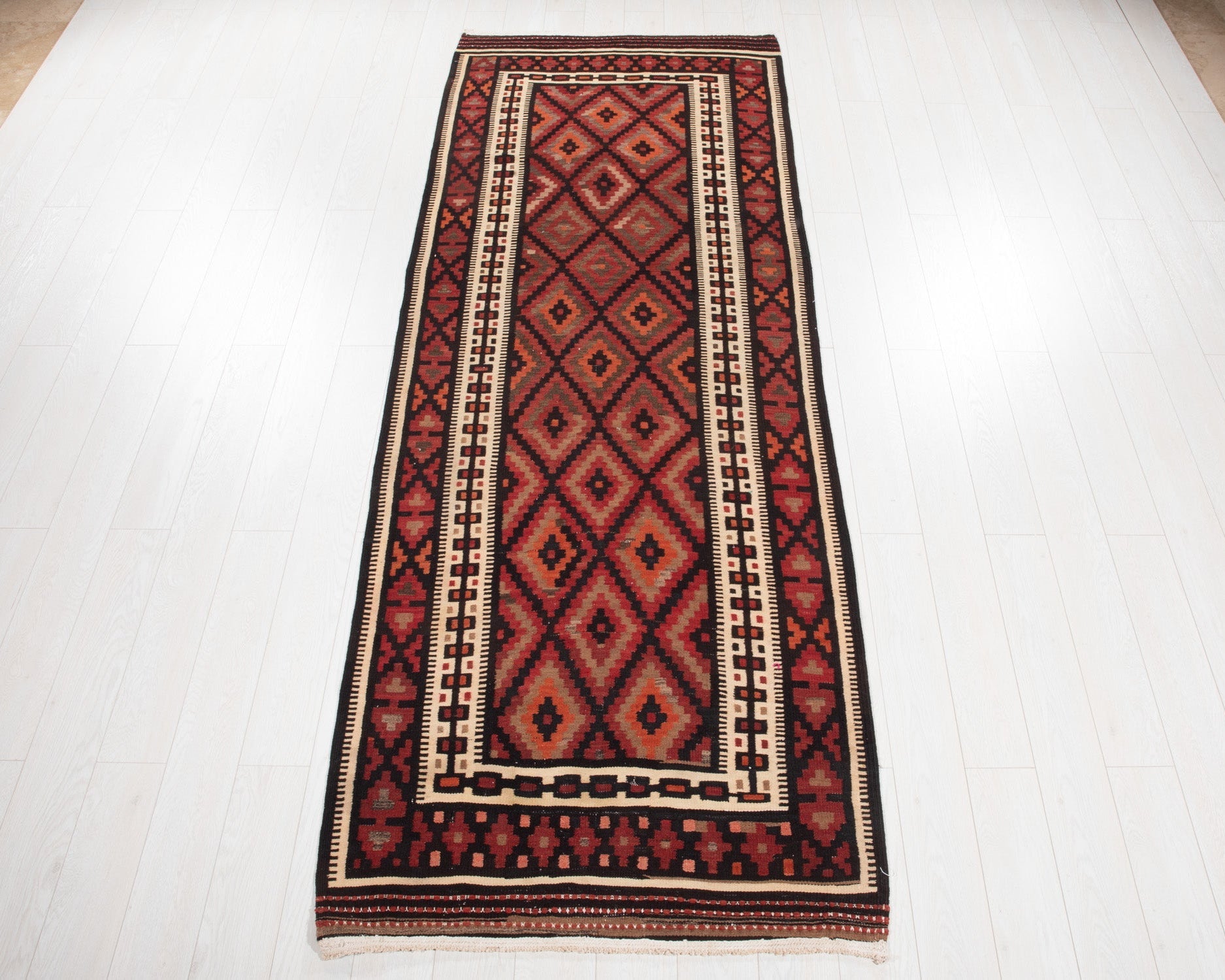 Full view of the vintage Persian kilim runner in red and orange geometric diamonds.