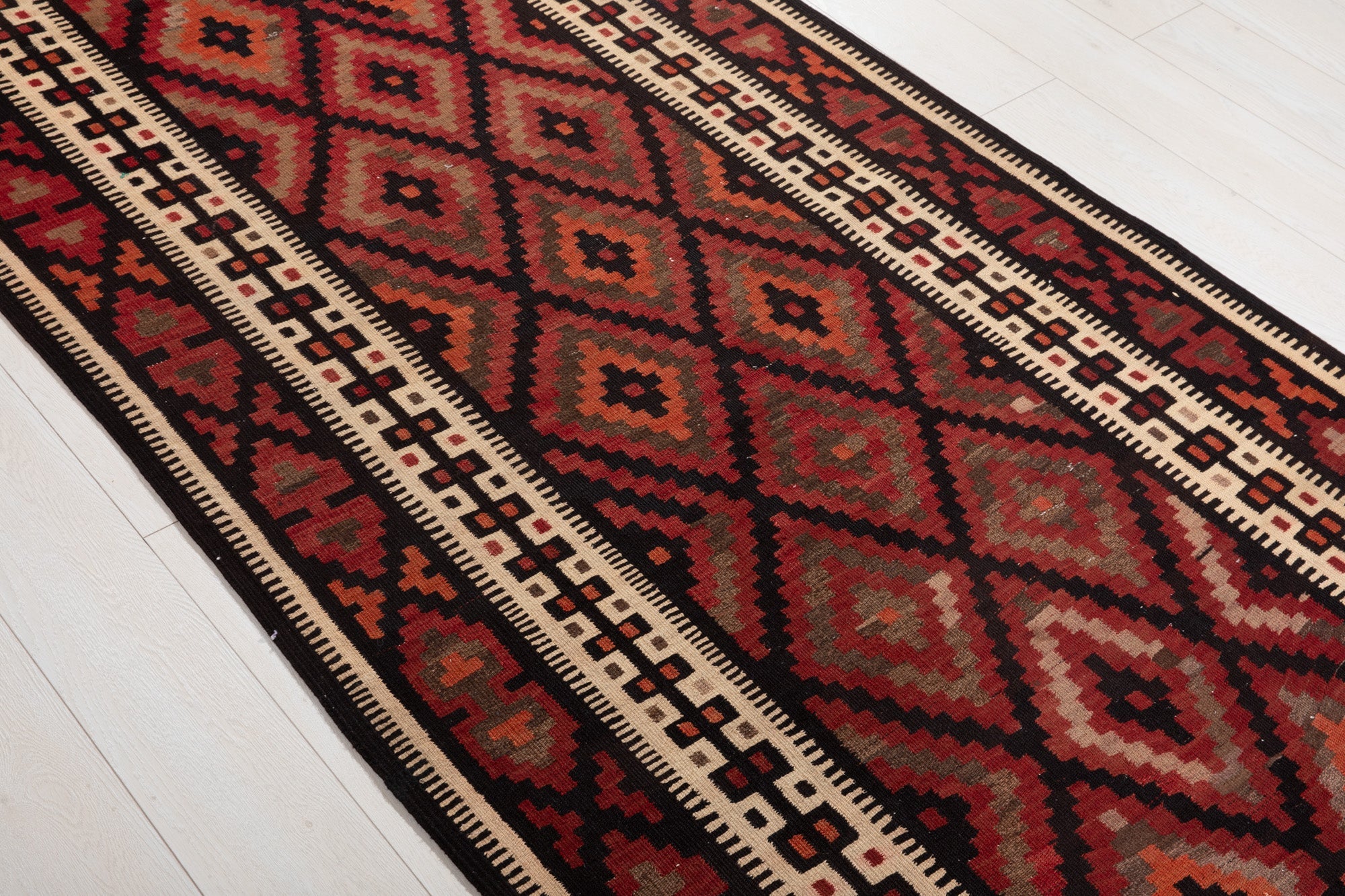 Diagonal close view of the kilim's red and orange diamond lattice pattern.
