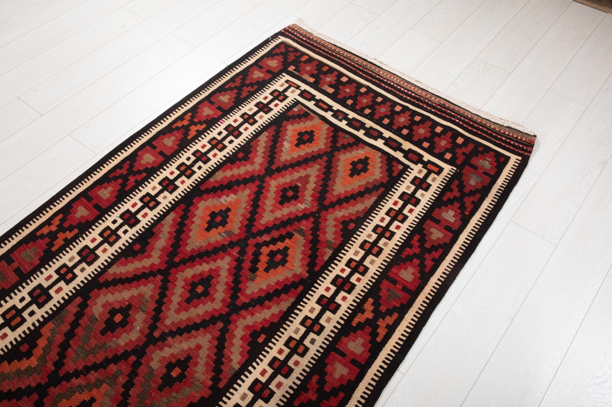Floor-level angled view of the kilim's diamond pattern and fringed edge.