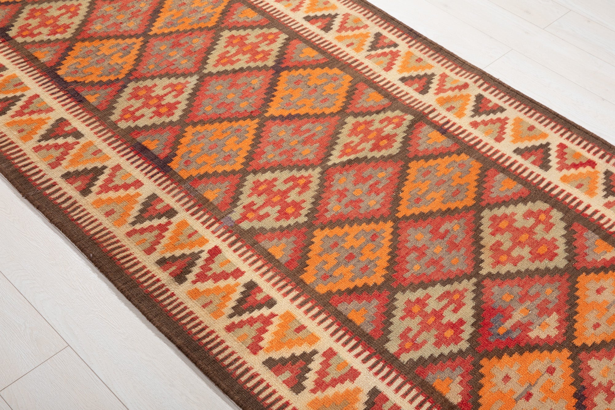 Diagonal close view of the kilim's diamond squares in red, orange and gray.