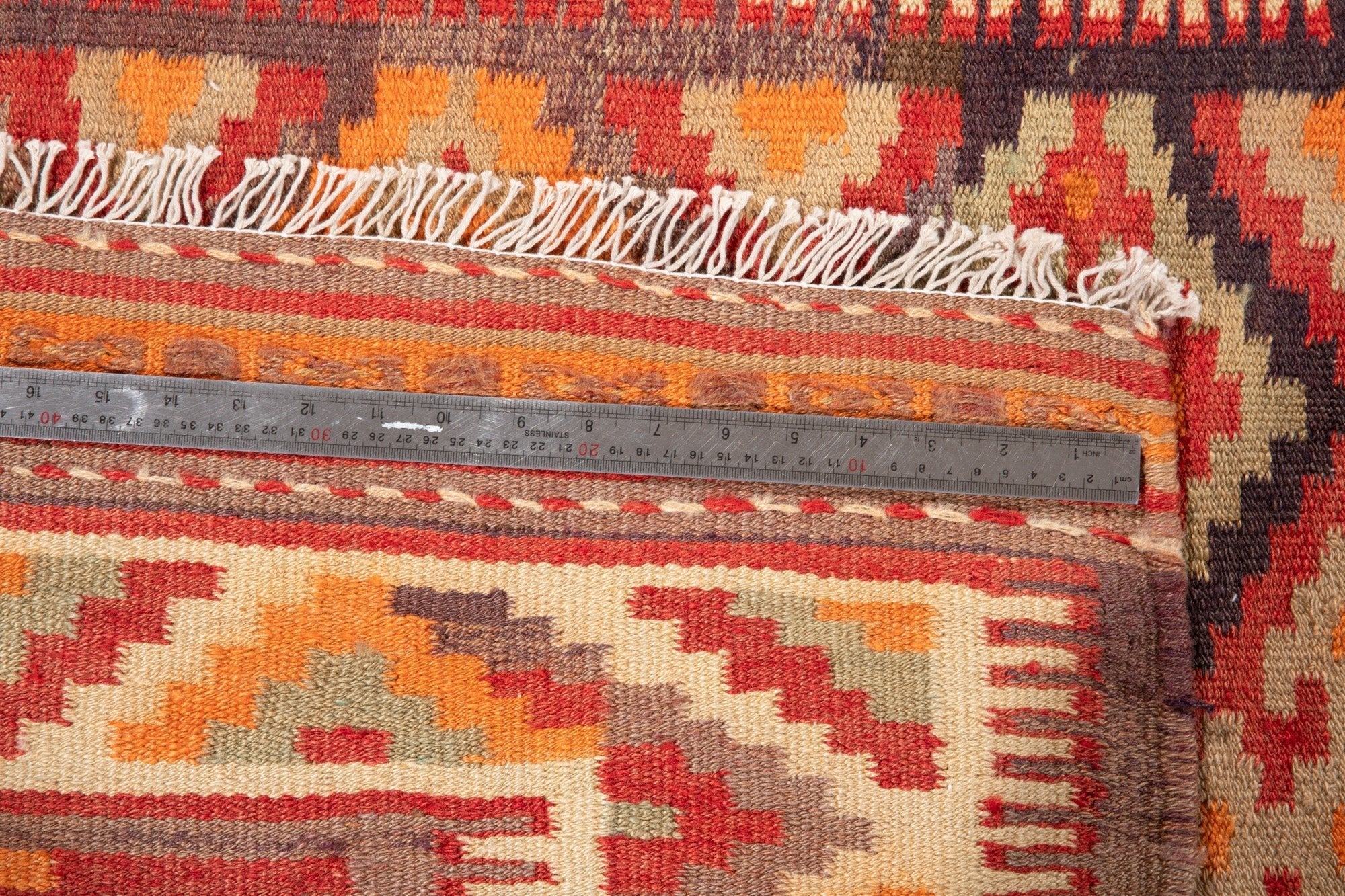 Ruler measuring the kilim's border width next to its fringe.