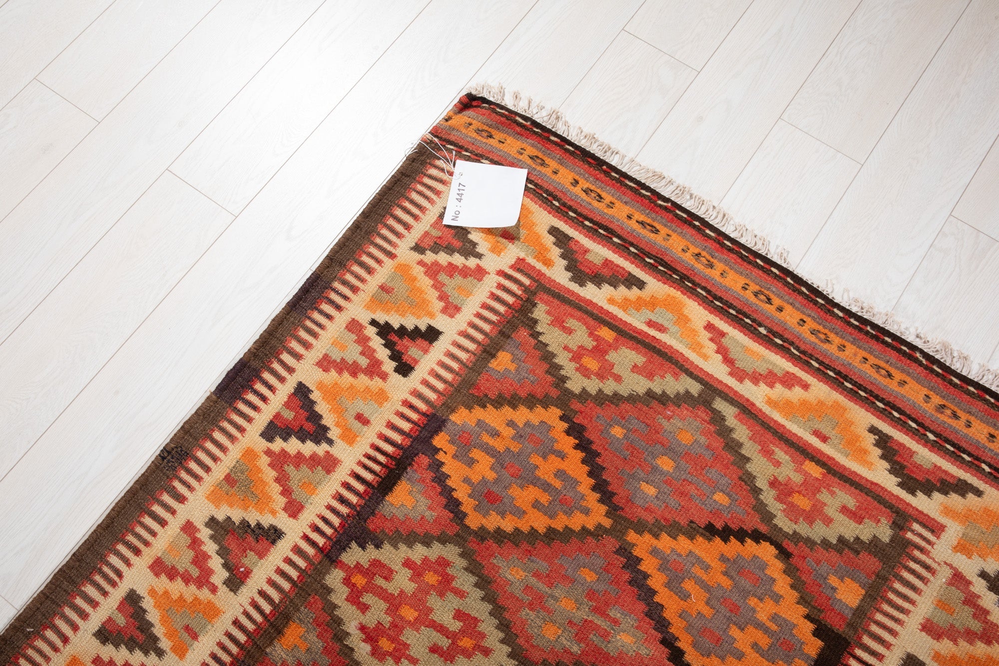 Corner of the vintage Persian kilim runner with an attached inventory identification tag.