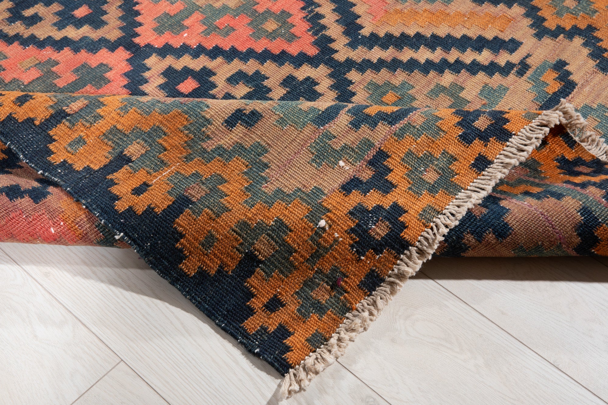 Corner of the runner folded up, showing its diamond pattern and fringed edge.