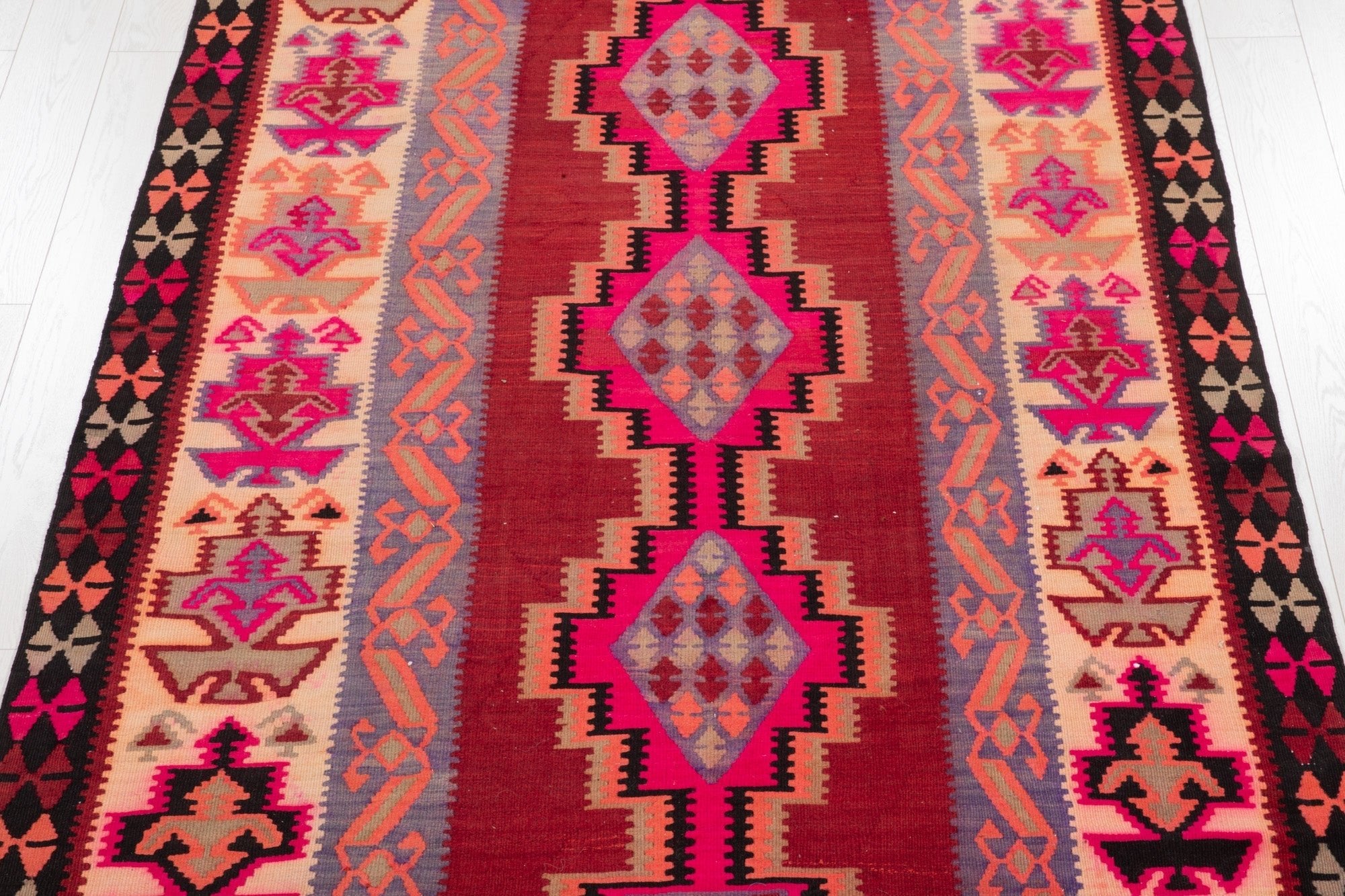 Top-down view of the kilim's diamond medallions and floral motifs in pink and red.