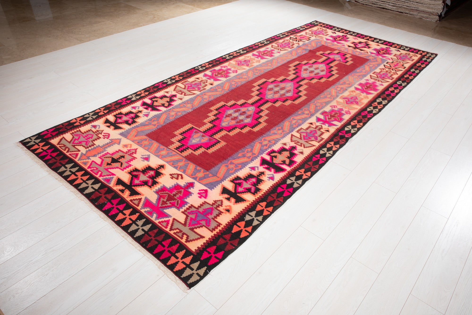 Angled view of the Persian Shiraz kilim's pink diamond medallions on the showroom floor.