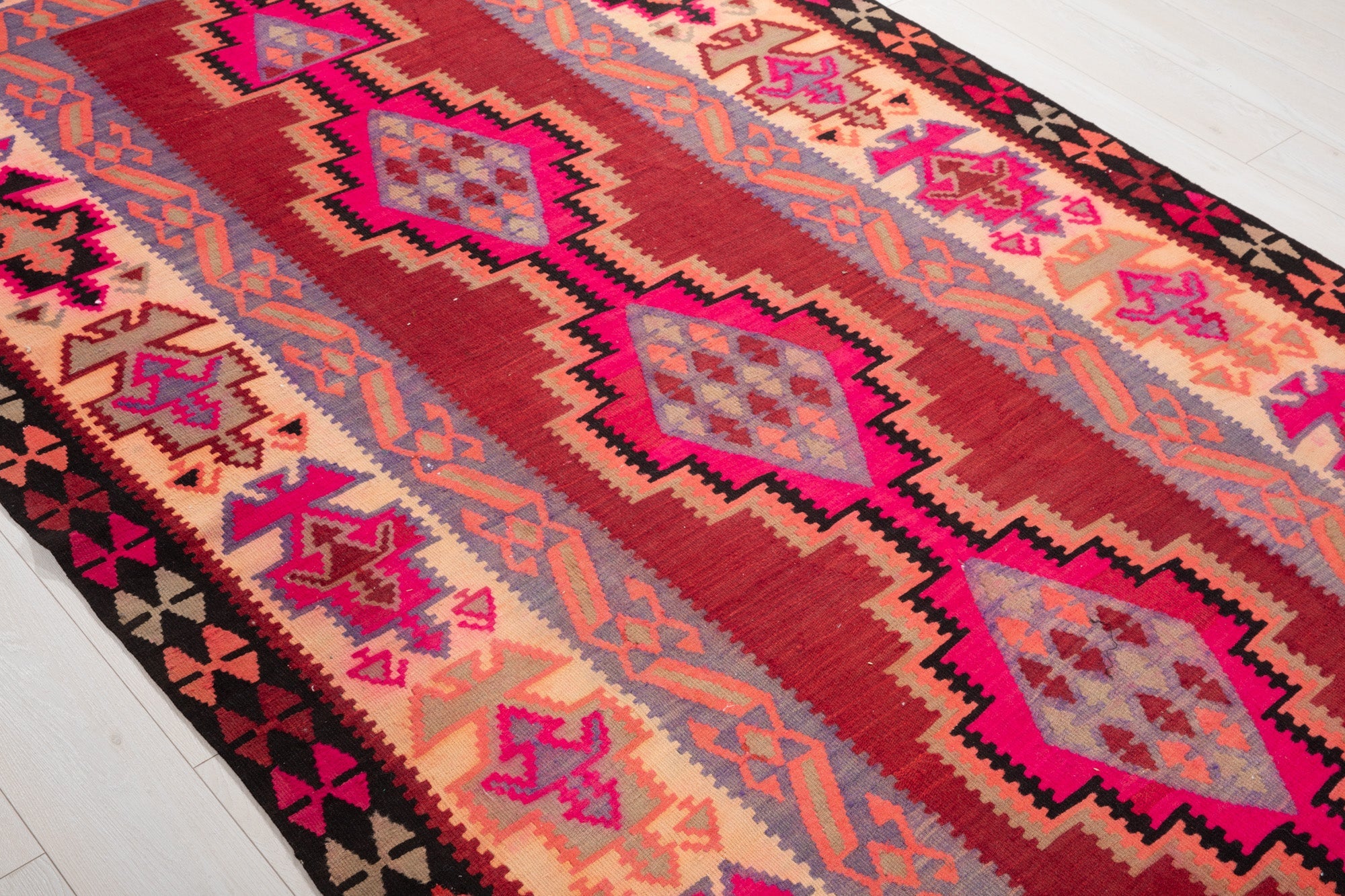 Diagonal close view of the kilim's pink diamond medallions in a row.