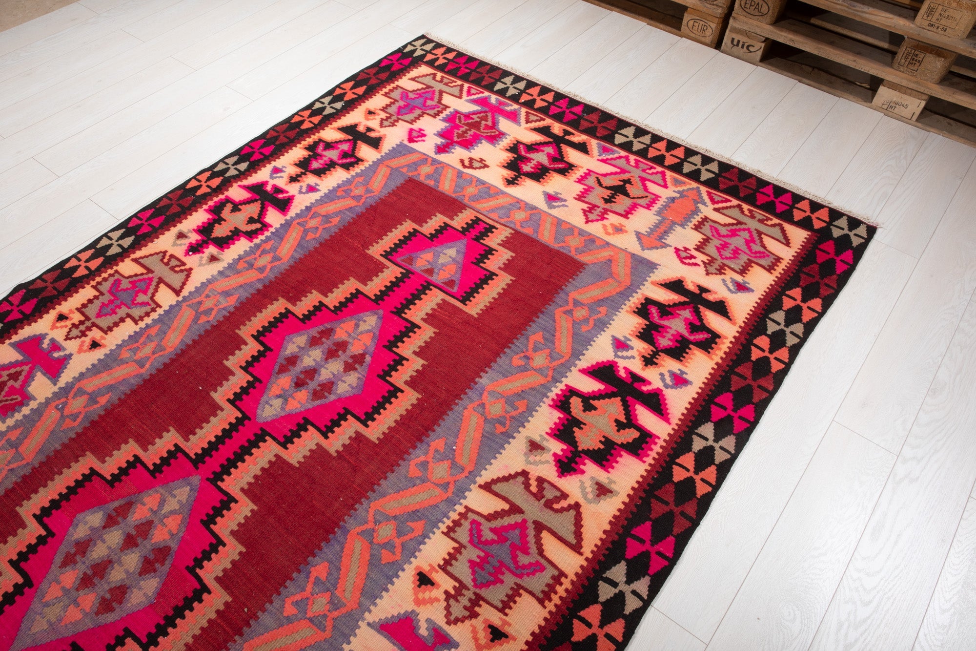 Warehouse angle shot of the kilim rug's diamond medallions with pallets in the background.