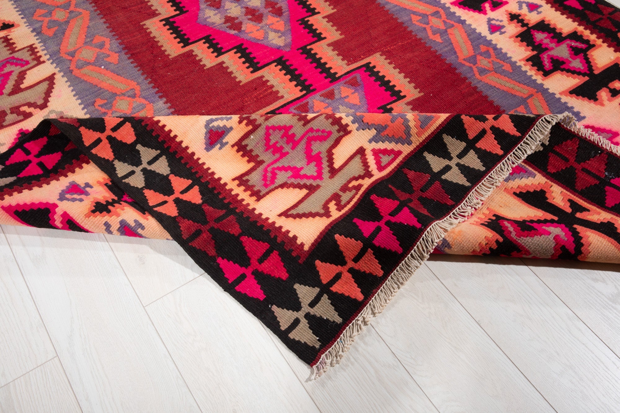 Corner of the kilim rug folded up, showing its triangle border and fringed edge.