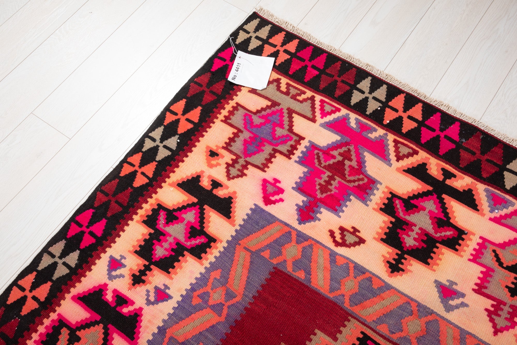 Corner of the vintage Persian Shiraz kilim rug with an attached inventory identification tag.