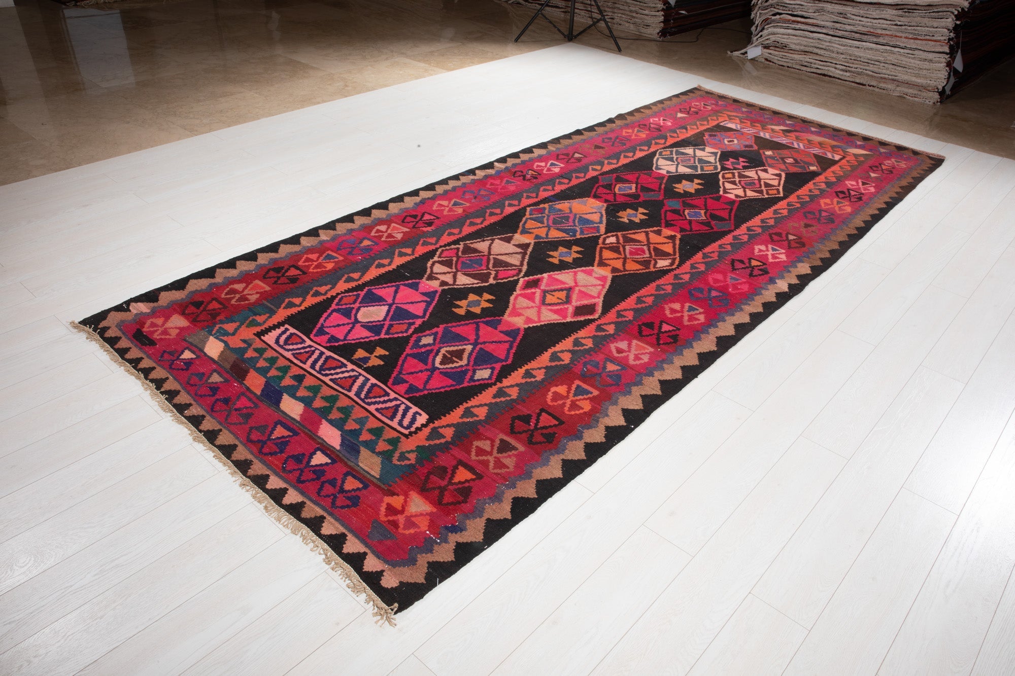 Angled view of the Persian kilim rug's red and black diamond medallions.
