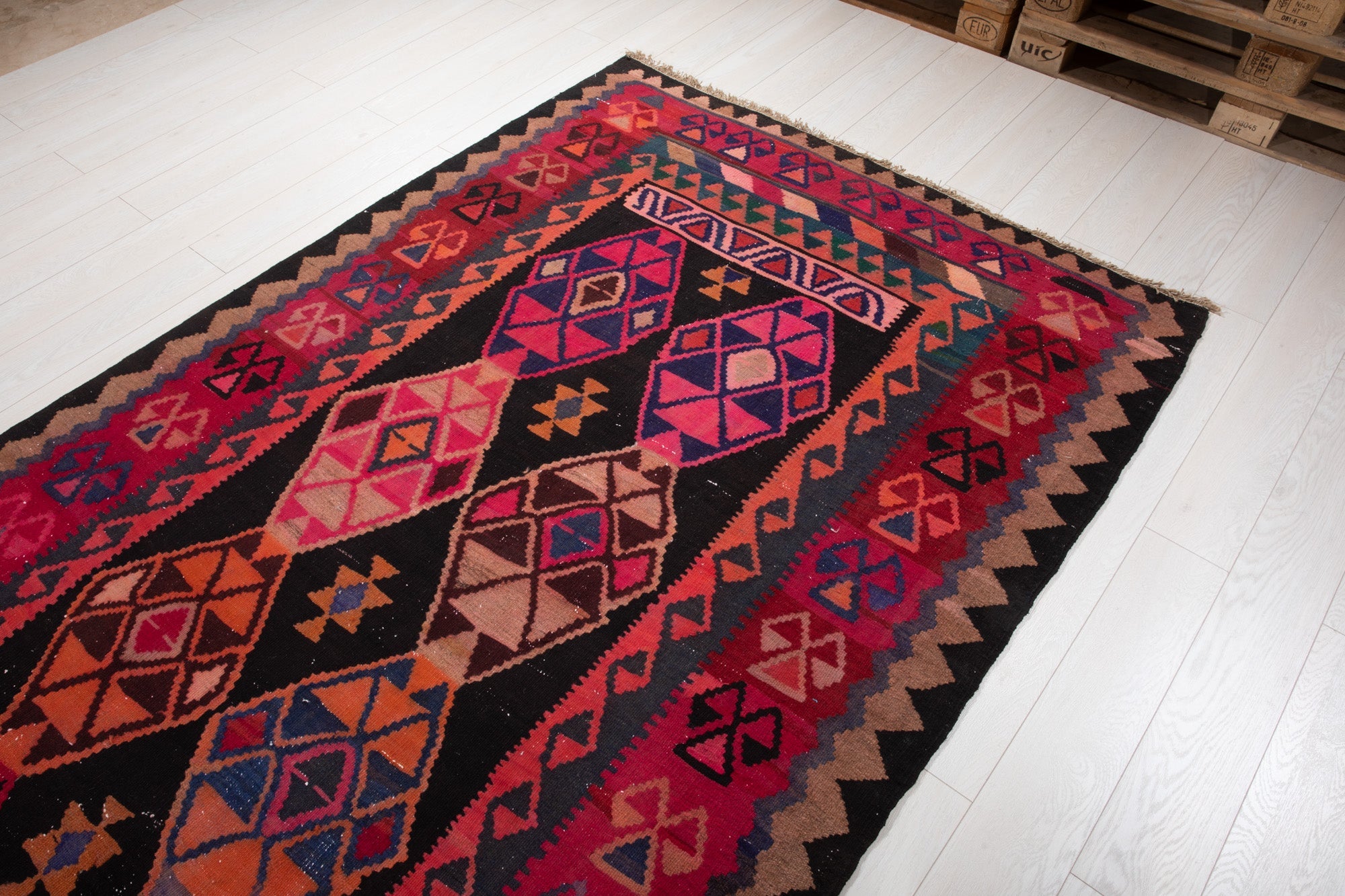 Warehouse angle shot of the kilim rug's diamond medallions with pallets in the background.