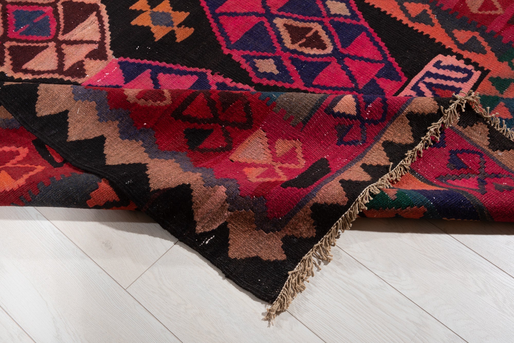 Corner of the kilim rug folded up, showing its triangle pattern and fringed edge.