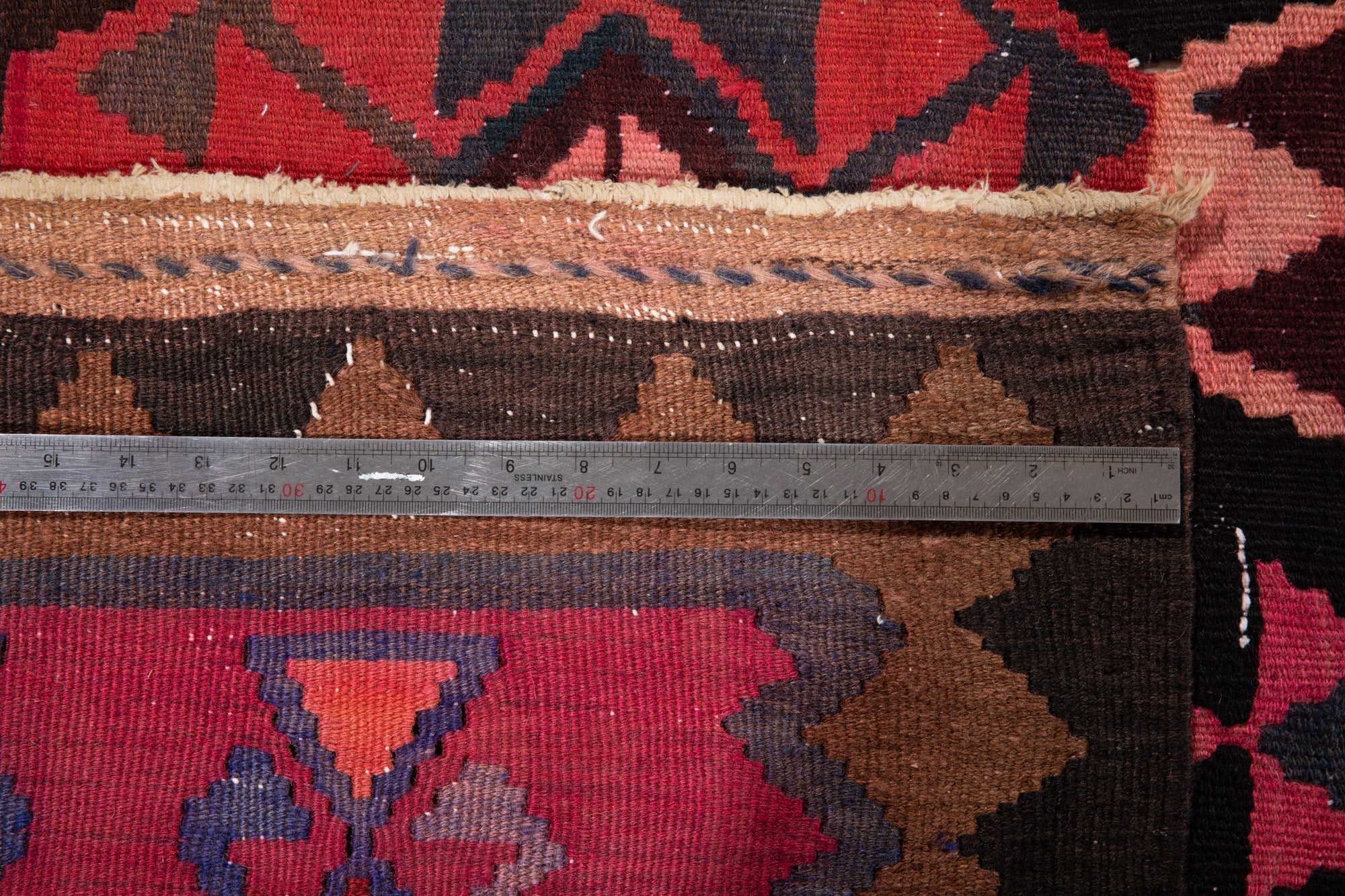 Ruler measuring the kilim's border width next to its fringe.