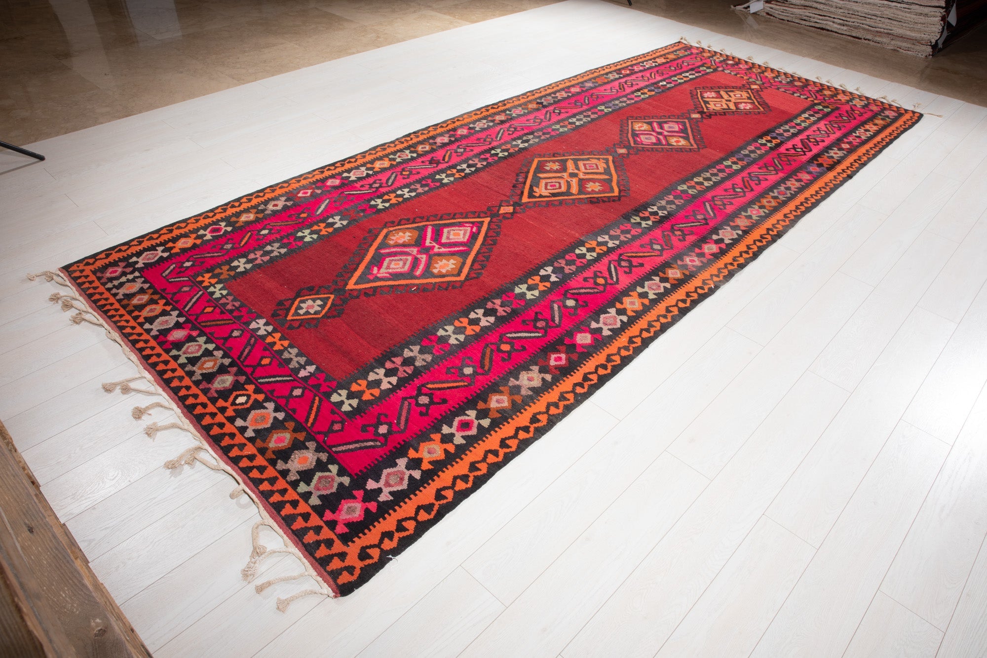 Angled view of the Persian kilim runner's red diamond medallions on a wood platform.
