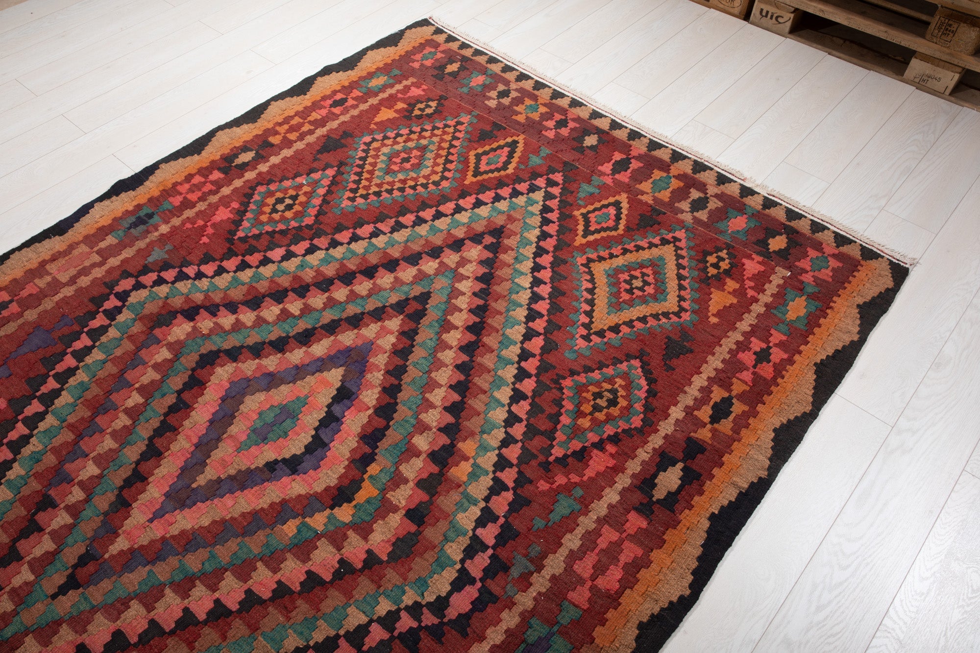 Warehouse angle shot of the kilim rug's diamond medallions with pallets in the background.