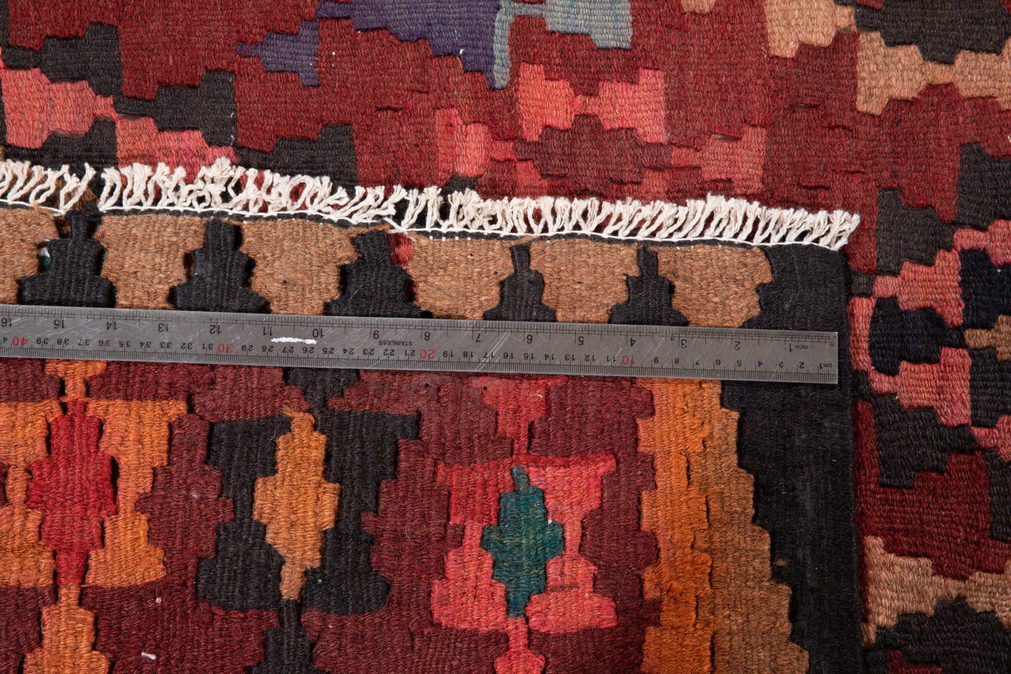 Ruler measuring the kilim's border width next to its fringe.