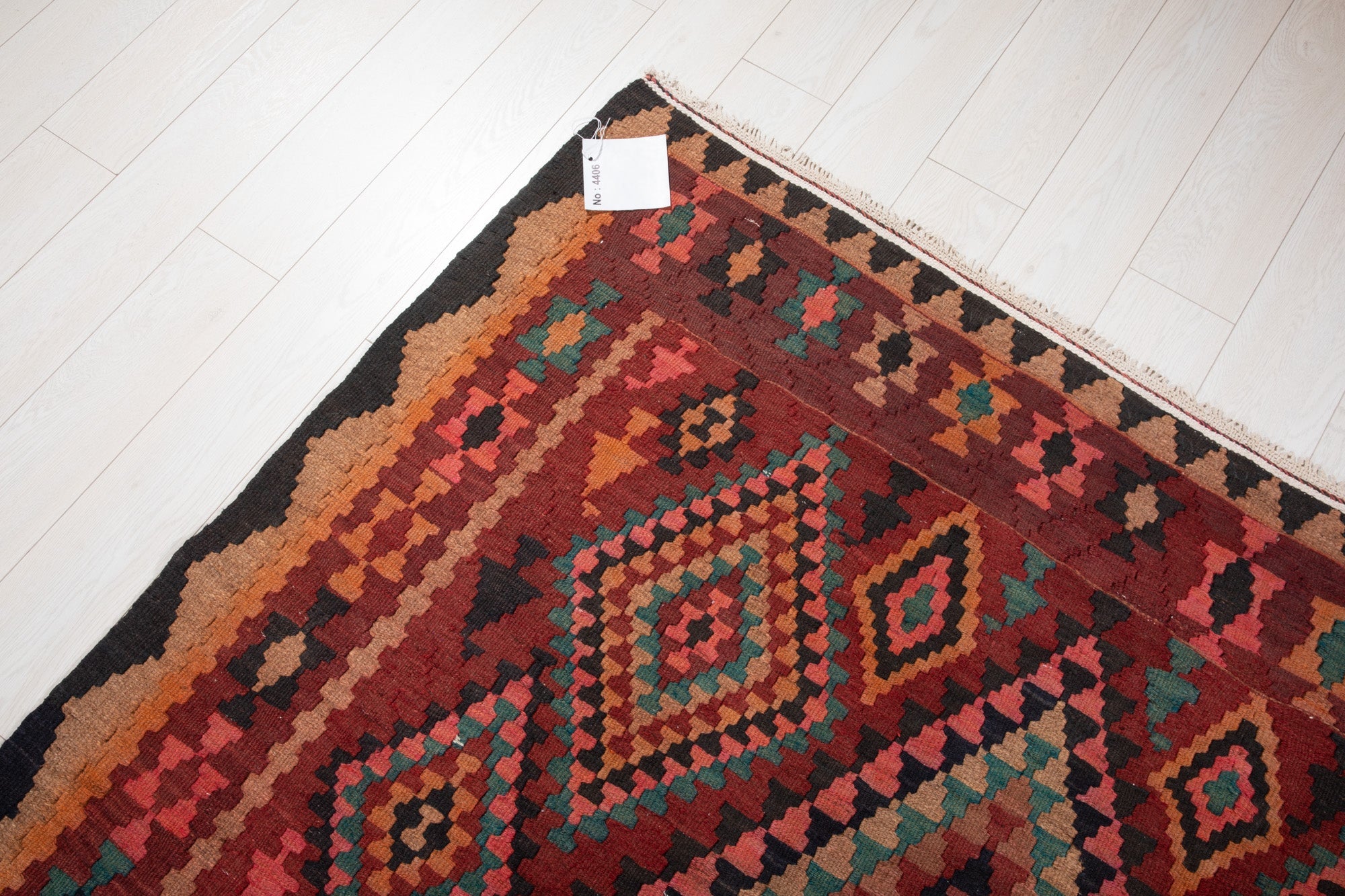 Corner of the vintage Shiraz Persian kilim rug with an attached inventory identification tag.