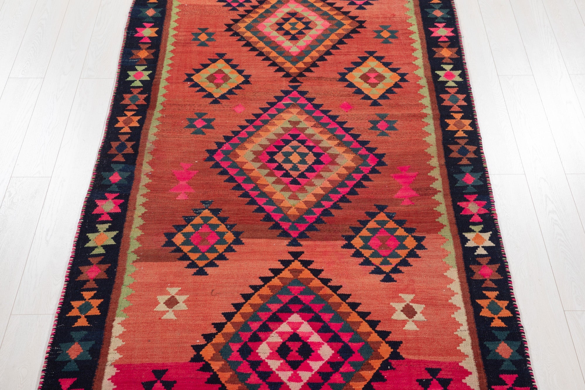 Top-down view of the kilim's stacked diamond medallions in orange and pink.