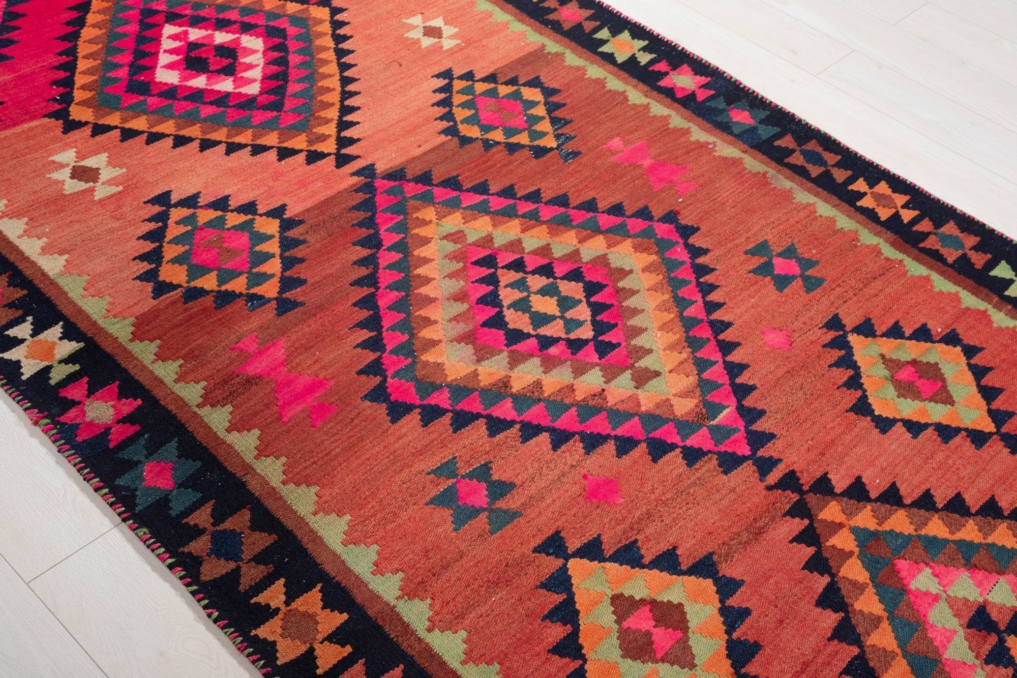 Diagonal close view of the kilim's diamond medallions on an orange field.
