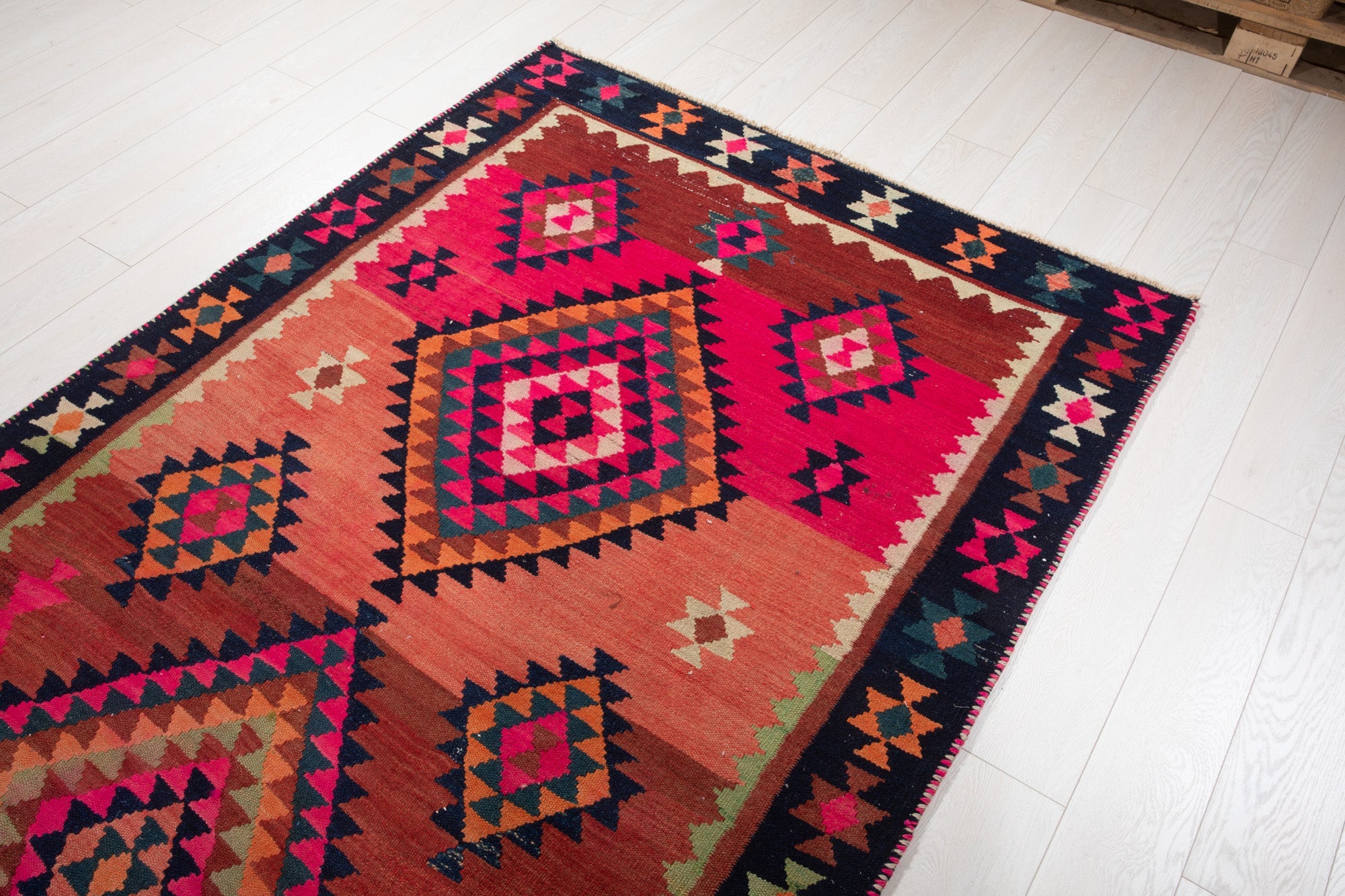 Warehouse angle shot of the kilim rug's diamond medallions with pallets in the background.